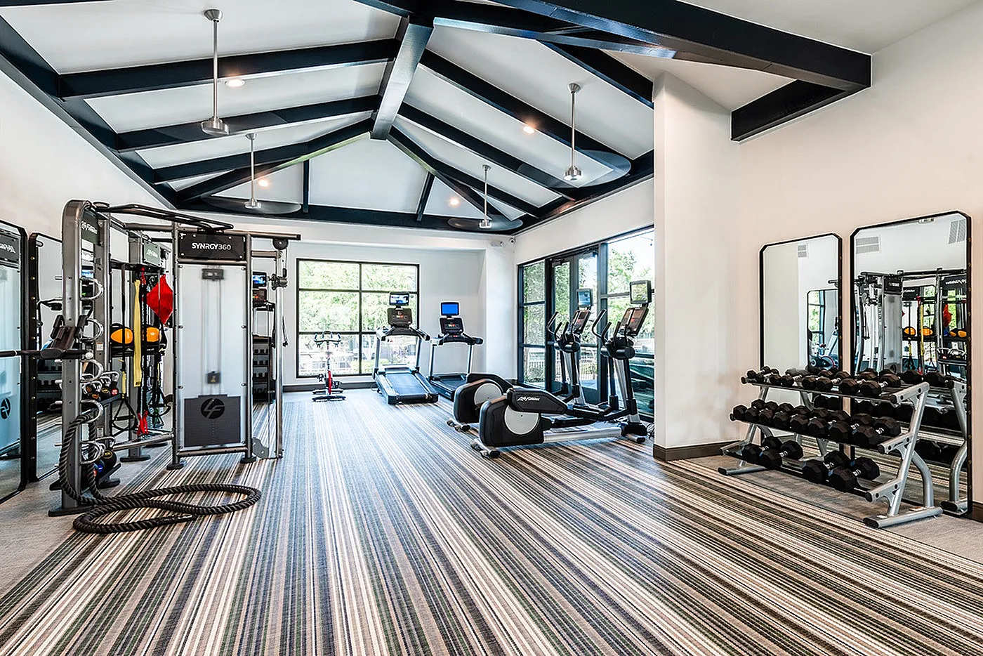 Modern fitness center with state-of-the-art equipment, sleek striped carpet, and large windows for natural light.