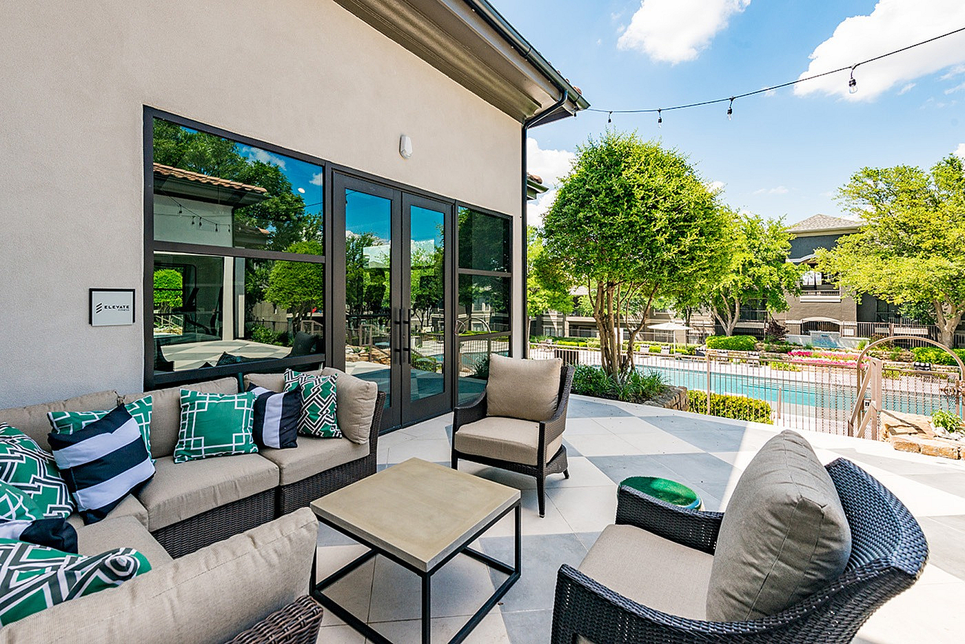 Charming outdoor patio with elegant wicker seating and vibrant cushions, overlooking a serene swimming pool surrounded by lush greenery.