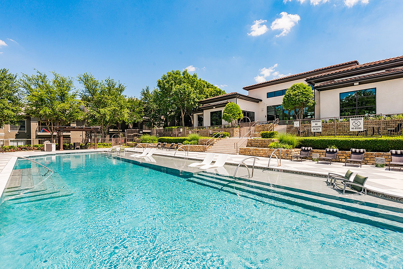 Luxurious apartment complex showcasing a sparkling outdoor pool, surrounded by lush greenery and modern architecture.