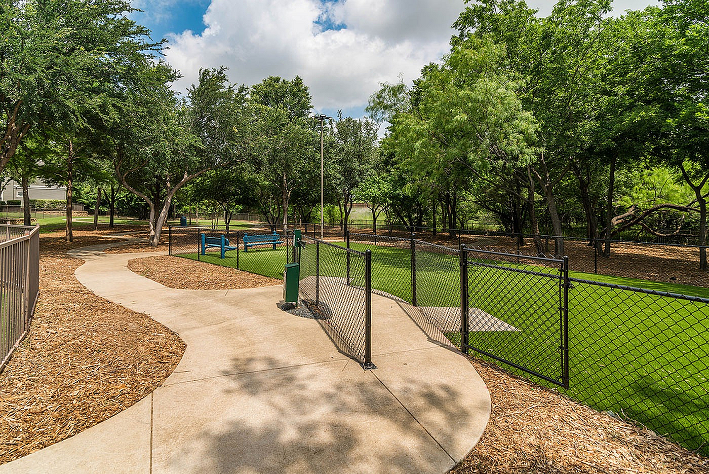 Scenic outdoor space featuring lush greenery, walking paths, and a fenced area perfect for relaxation and play.