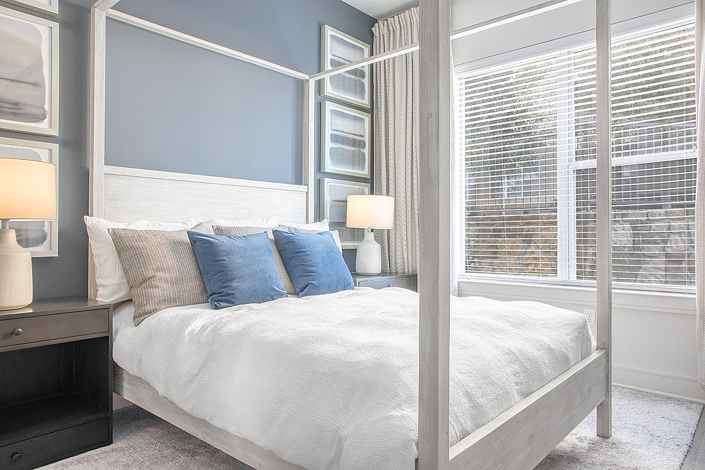 Elegant bedroom with a cozy white canopy bed, plush pillows, and soft lighting, featuring large windows for natural light.