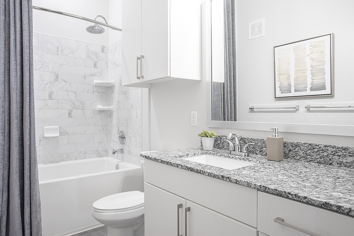 Elegant bathroom featuring a modern granite countertop, white cabinetry, and a luxurious tiled bathtub with a rainfall showerhead.