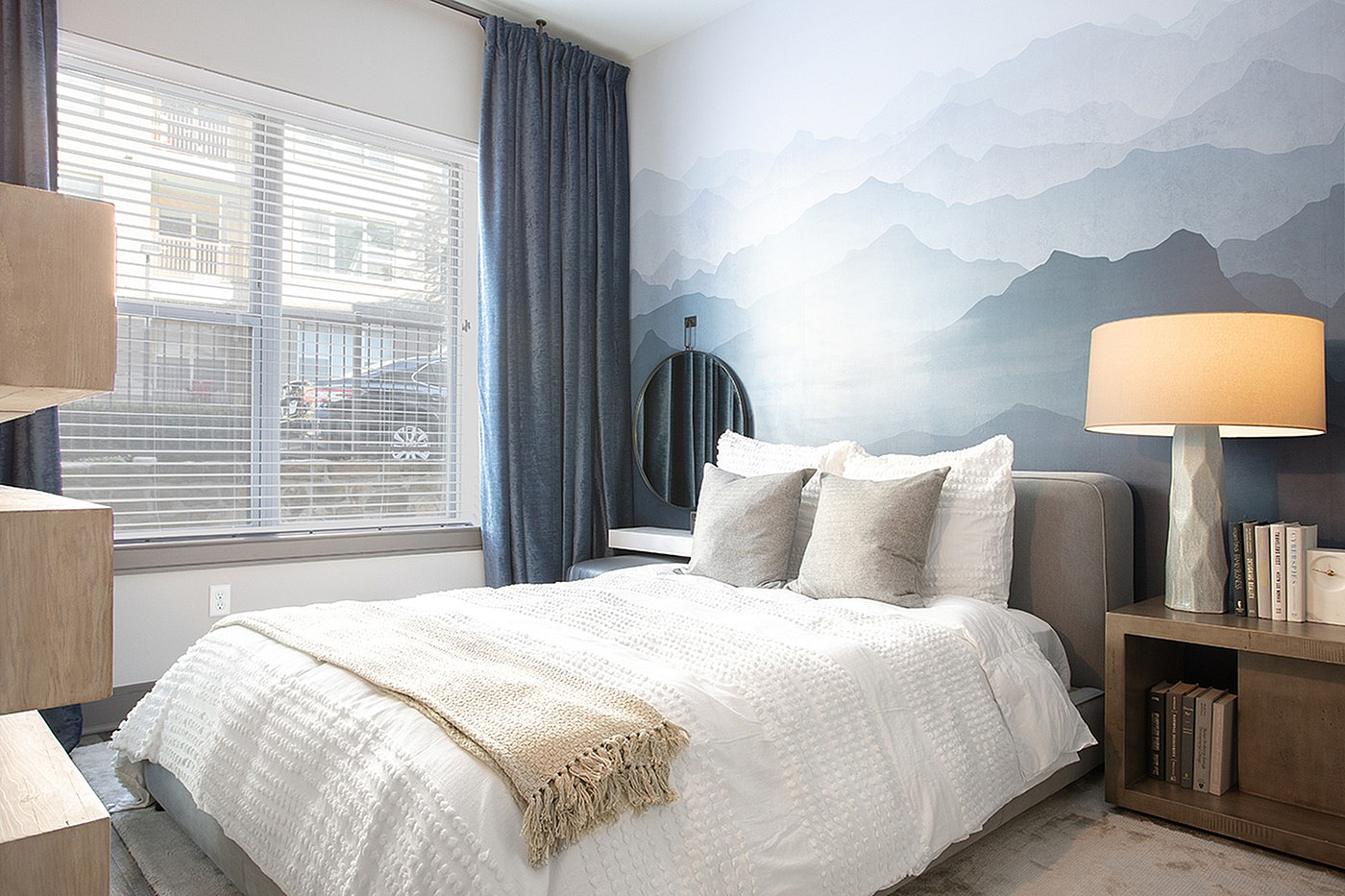 Serene bedroom with soft lighting, featuring a cozy bed, elegant side table, and artistic mountain-themed wall design.