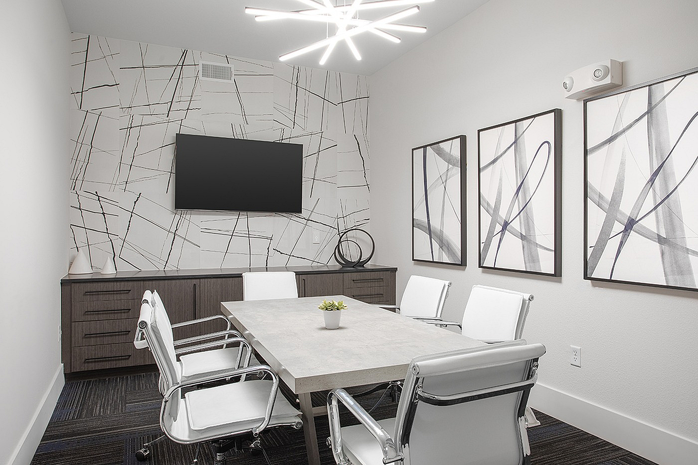 Modern conference room with chic geometric decor, sleek table, and stylish white chairs under contemporary lighting.