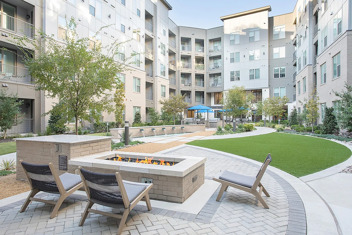 Inviting apartment courtyard with a cozy fire pit, stylish seating, lush green landscaping, and modern architecture.