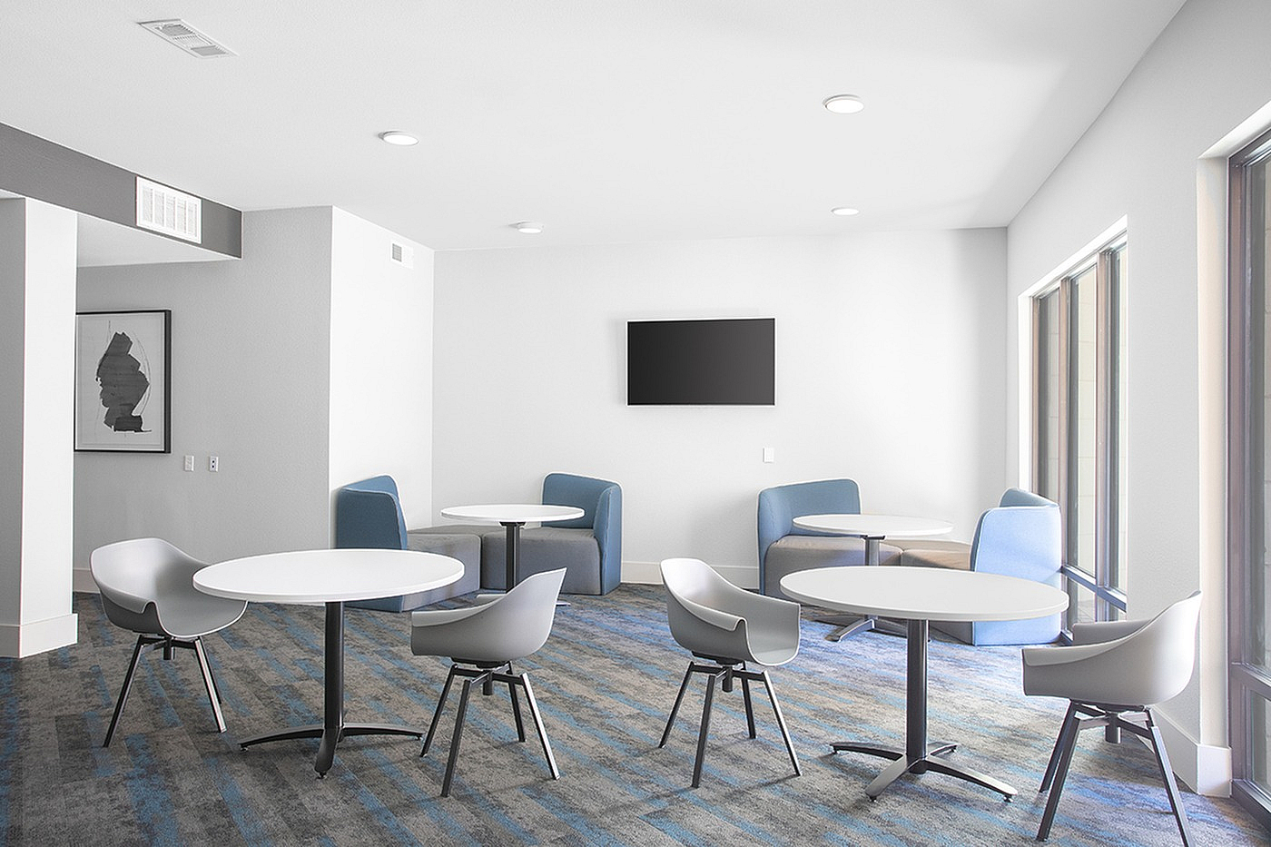 Bright and modern communal lounge area with sleek tables, ergonomic chairs, and large windows for natural light.