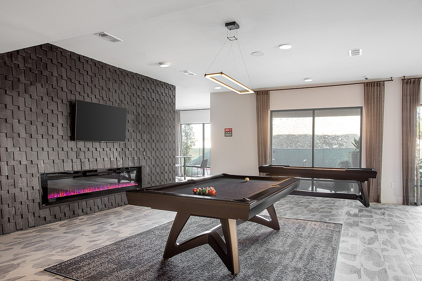 Contemporary game room with modern pool table, sleek fireplace, and large windows for natural light.