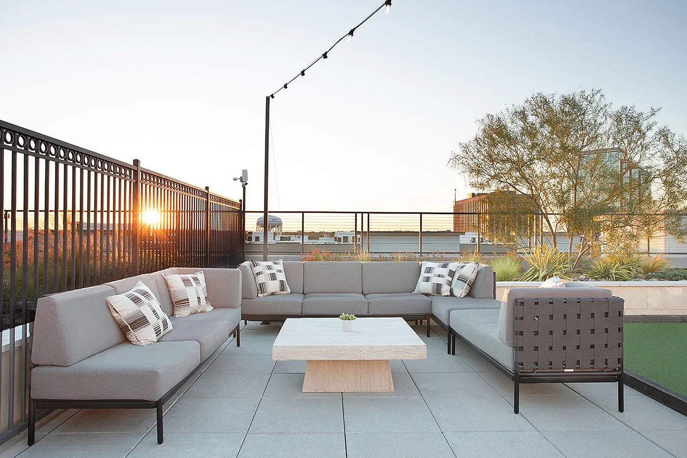 Chic rooftop patio with modern gray seating, a stylish table, and stunning cityscape views at sunset.