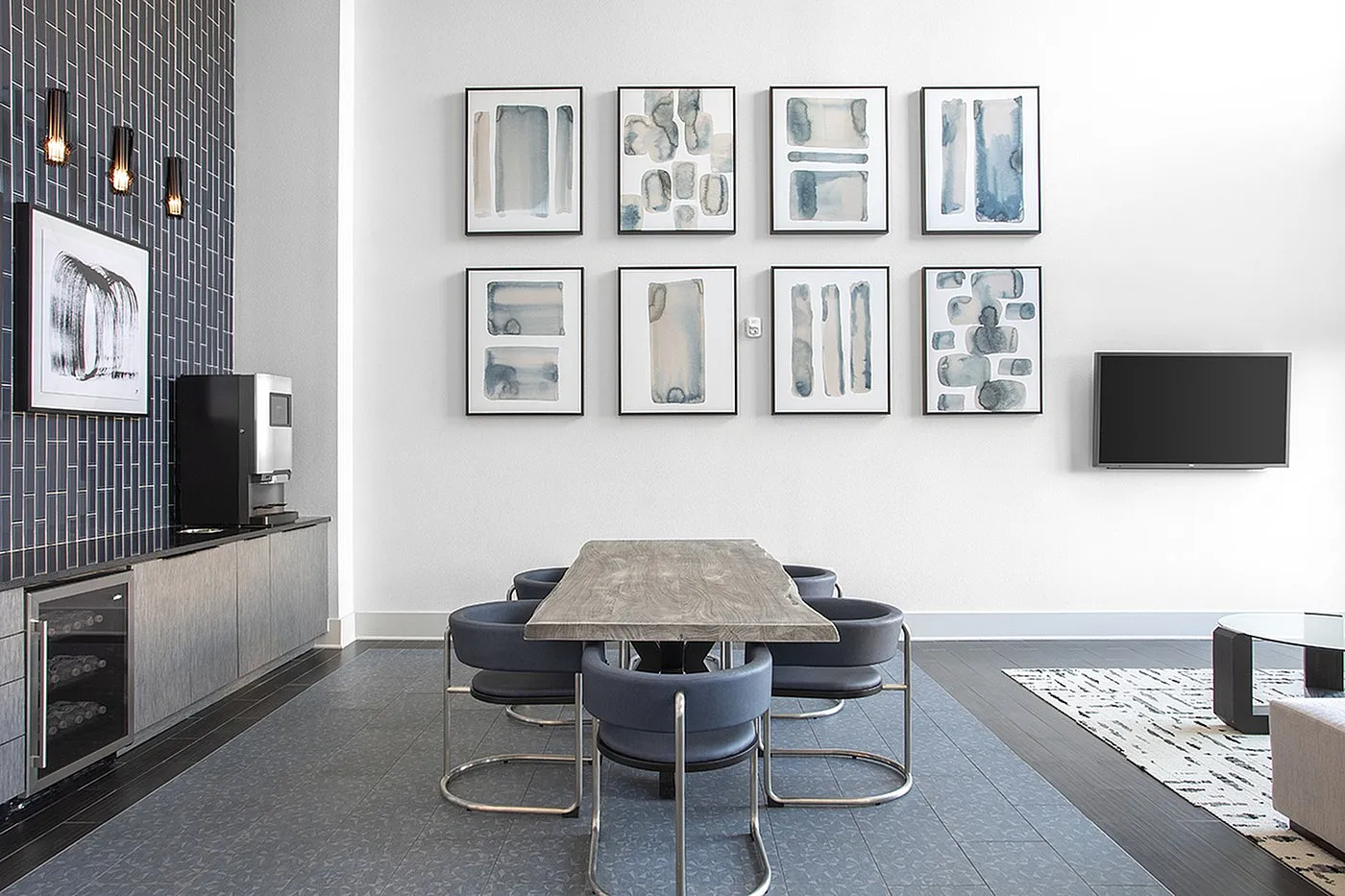 Modern dining area featuring a sleek wooden table with stylish blue chairs, complemented by contemporary art pieces and a wall-mounted TV.