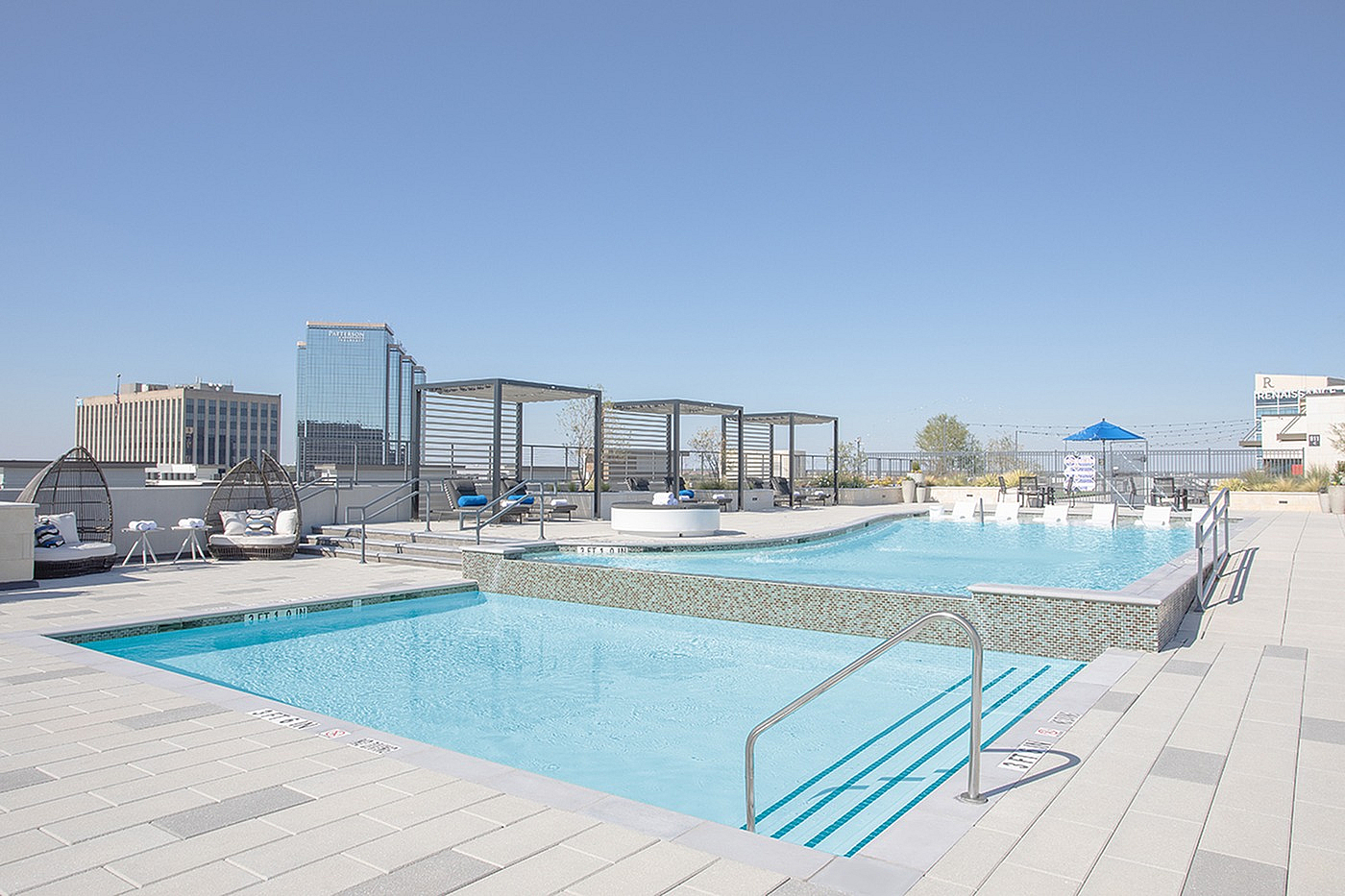 Luxury rooftop pool with chic lounge chairs, modern cabanas, and stunning city skyline views under a clear blue sky.