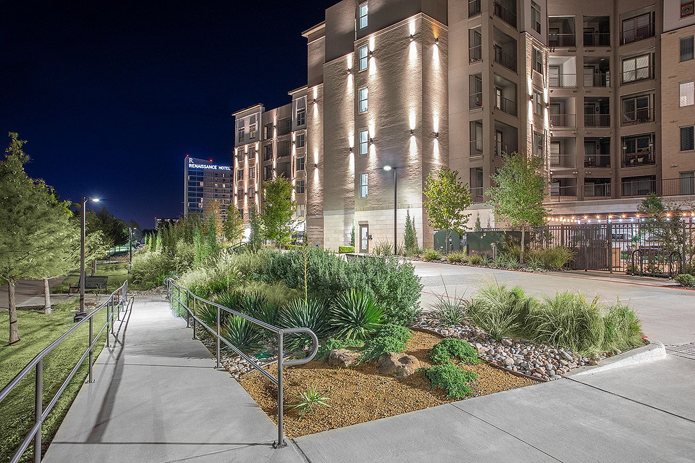 Elegant nighttime view of a modern apartment complex with beautifully landscaped paths, highlighted by strategic lighting.