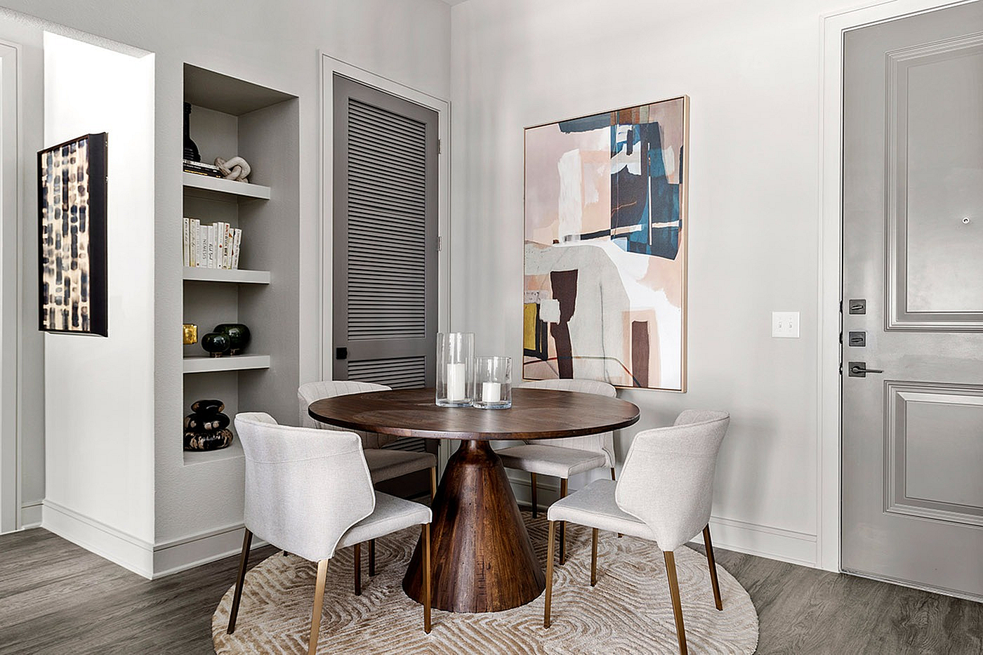 Elegantly designed dining nook featuring a round wooden table, four modern chairs, and contemporary artwork on light-toned walls.