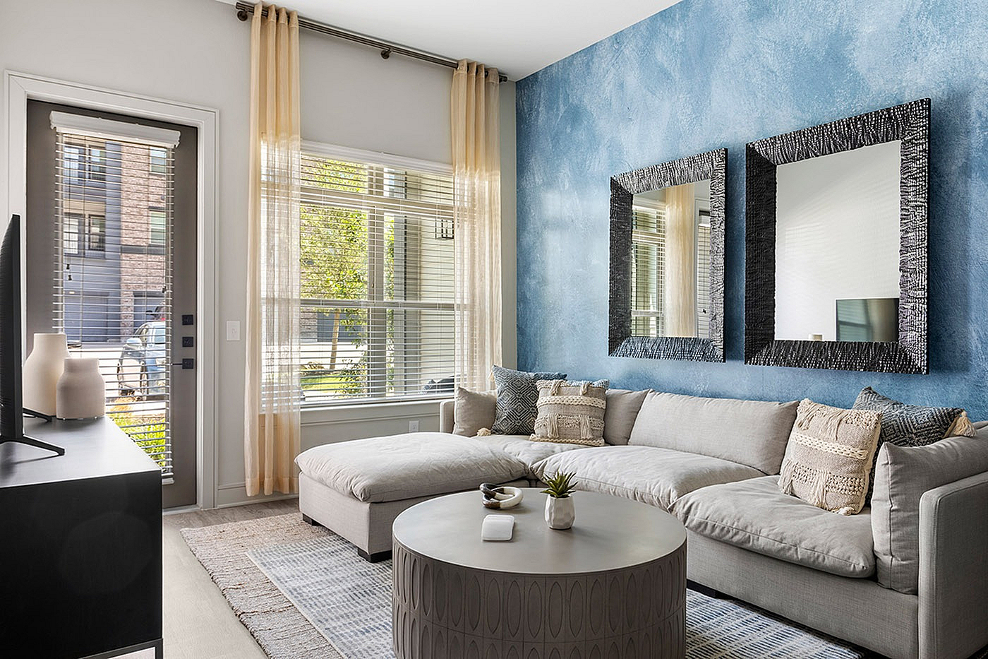 Chic living room with elegant decor, featuring a plush sectional sofa, stylish round coffee table, and a serene blue accent wall with modern mirrors.