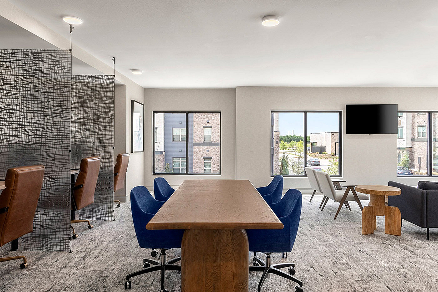Modern communal workspace featuring elegant wooden table, stylish blue and brown chairs, and expansive windows letting in natural light.
