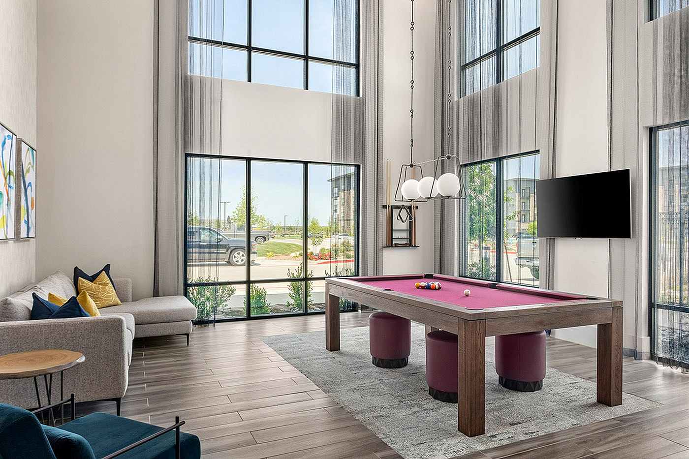 Elegant game room with high ceilings, featuring a stylish purple pool table and cozy seating, enhanced by floor-to-ceiling windows providing abundant natural light.