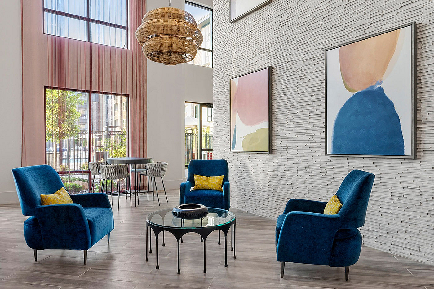 Chic and vibrant living space with plush blue chairs, modern art decor, and ample natural light through tall windows, offering a stylish and inviting atmosphere.