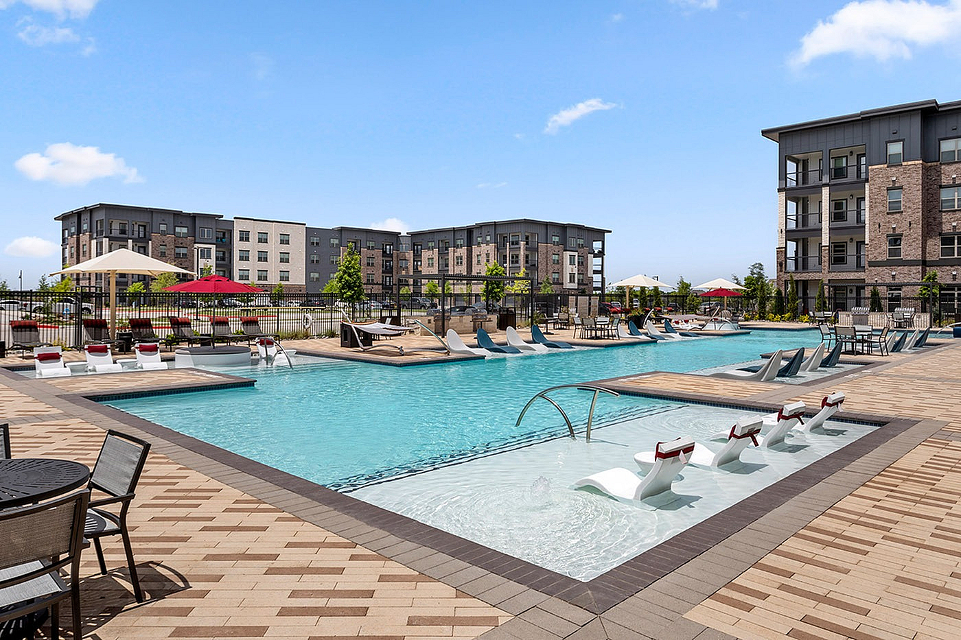 Modern apartment community with a luxurious swimming pool area featuring stylish lounge chairs, surrounded by beautifully designed multi-story buildings and vibrant landscaping.