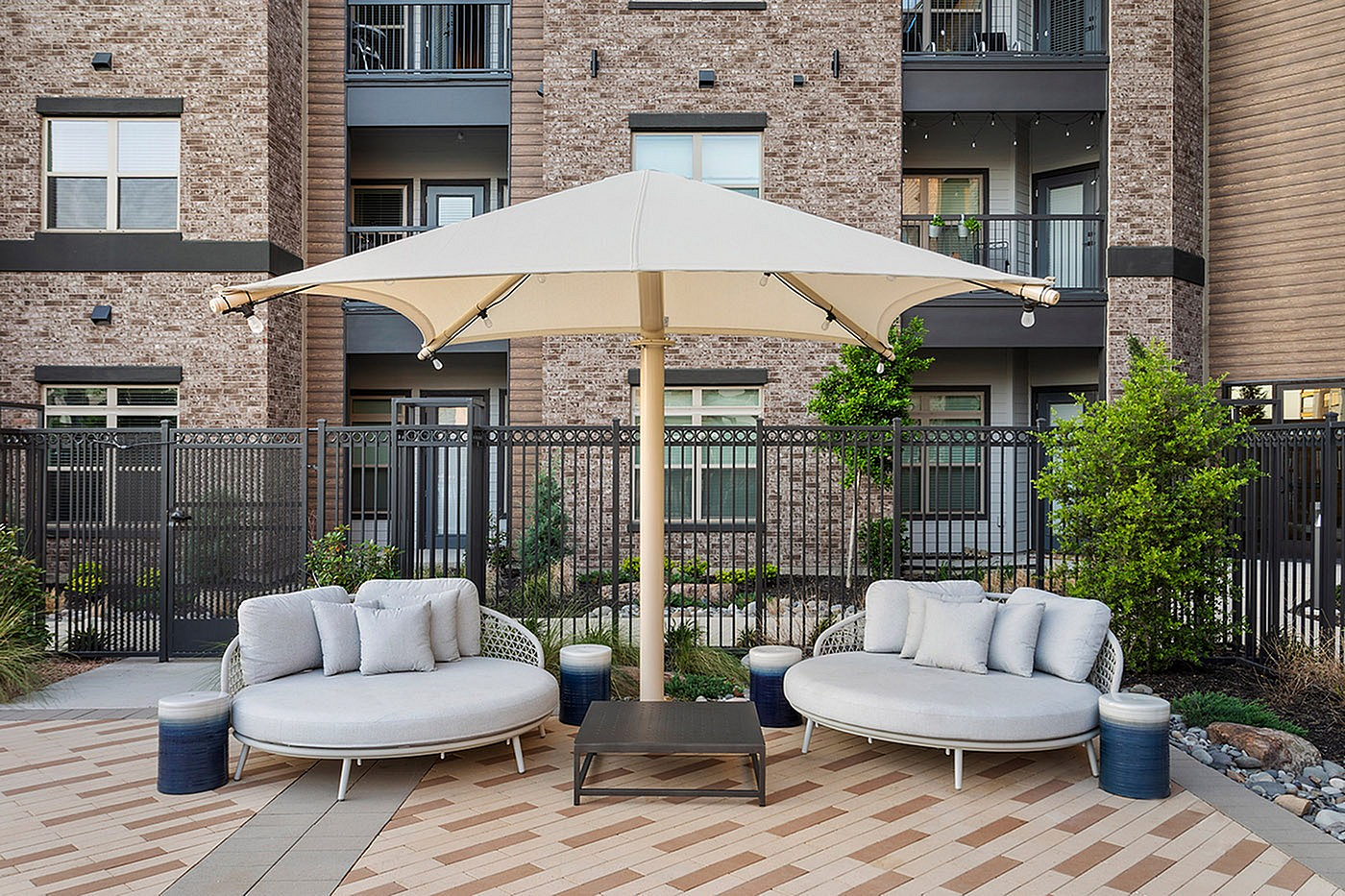 Chic outdoor patio space with cozy round seating, elegant umbrella, and modern building backdrop.