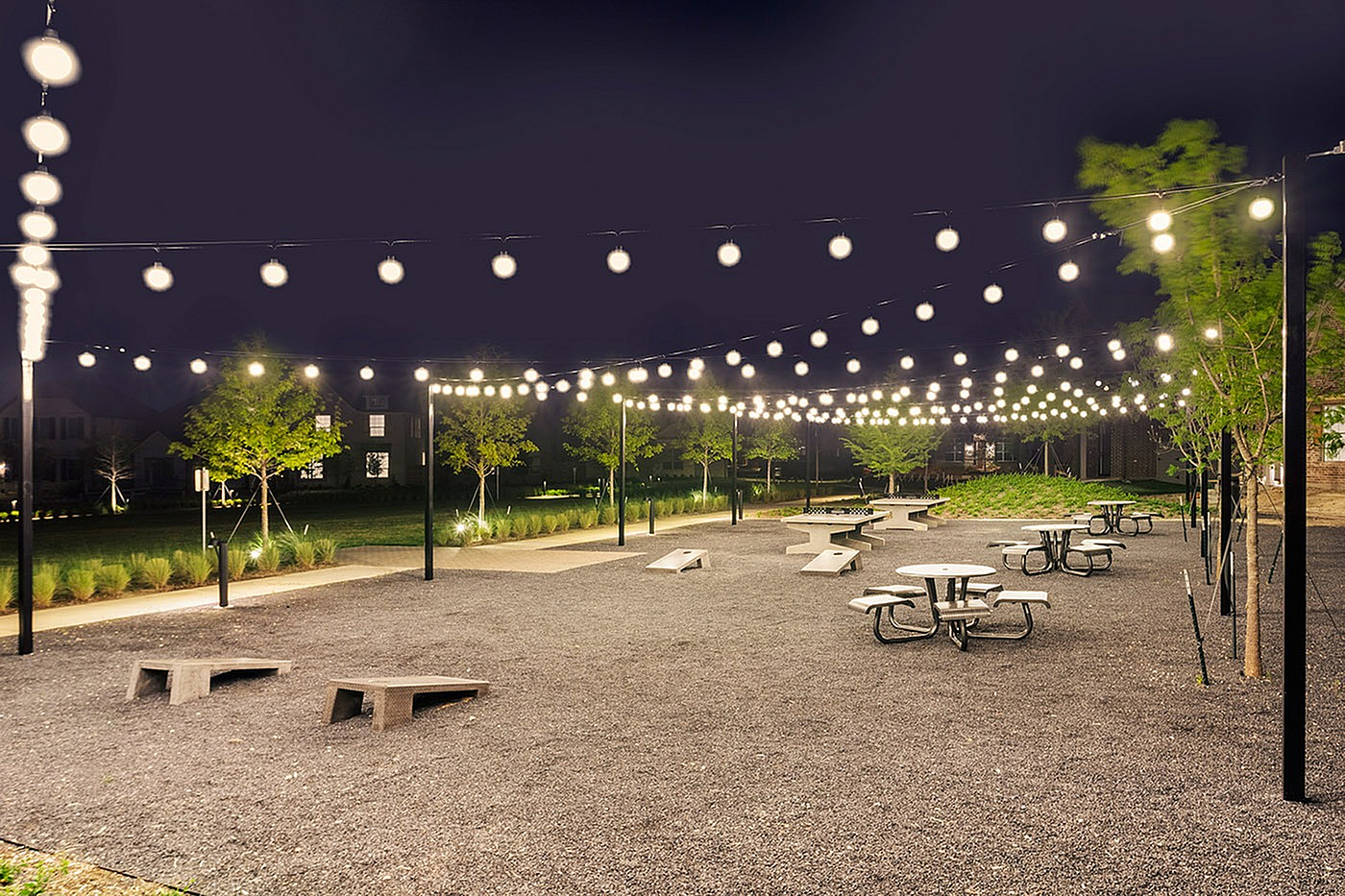 Charming outdoor space illuminated by strings of glowing lights, featuring picnic tables and inviting greenery, perfect for evening gatherings.