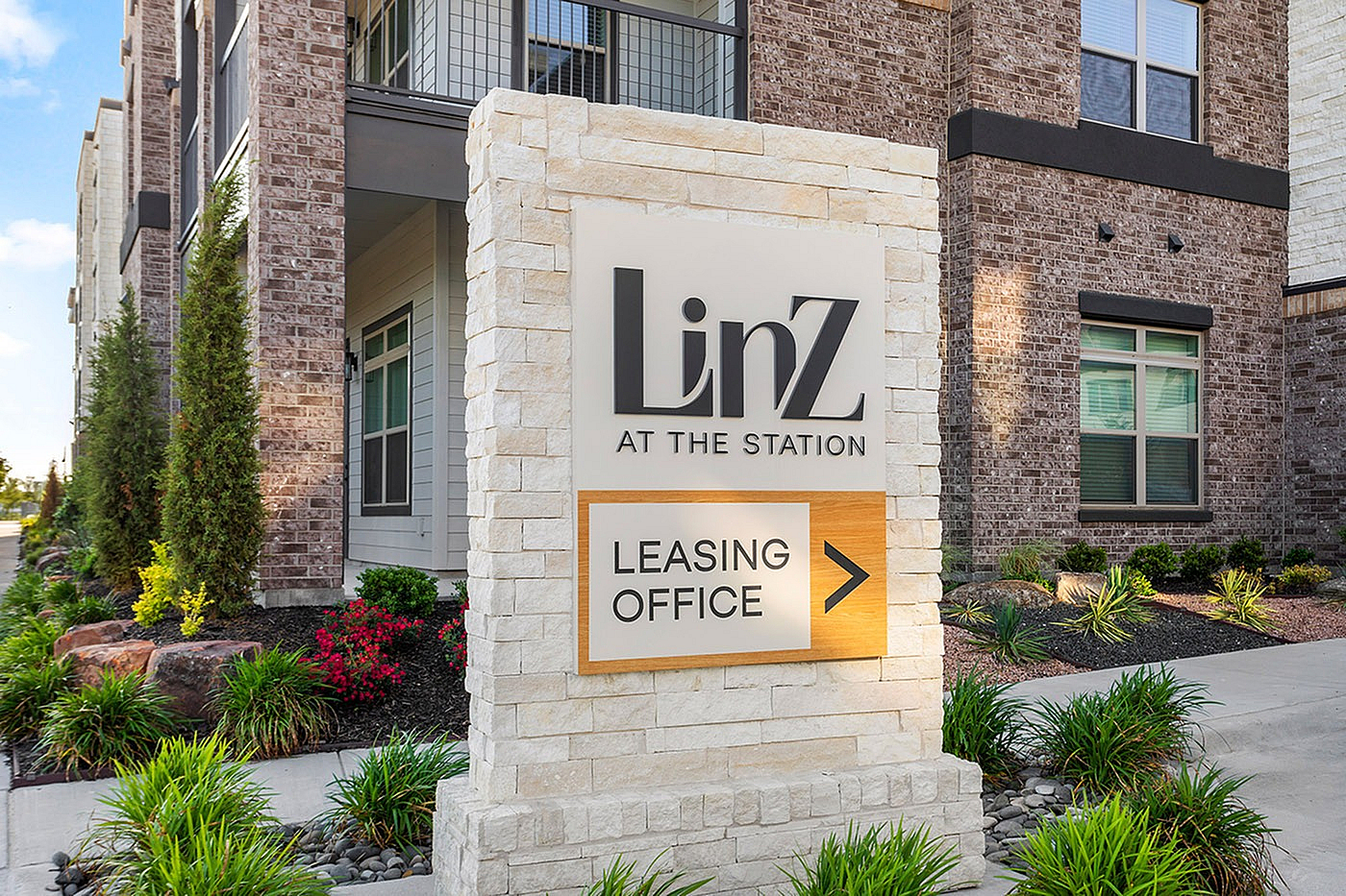 Inviting entrance to LinZ at the Station with a stylish leasing office sign amidst beautifully landscaped greenery.