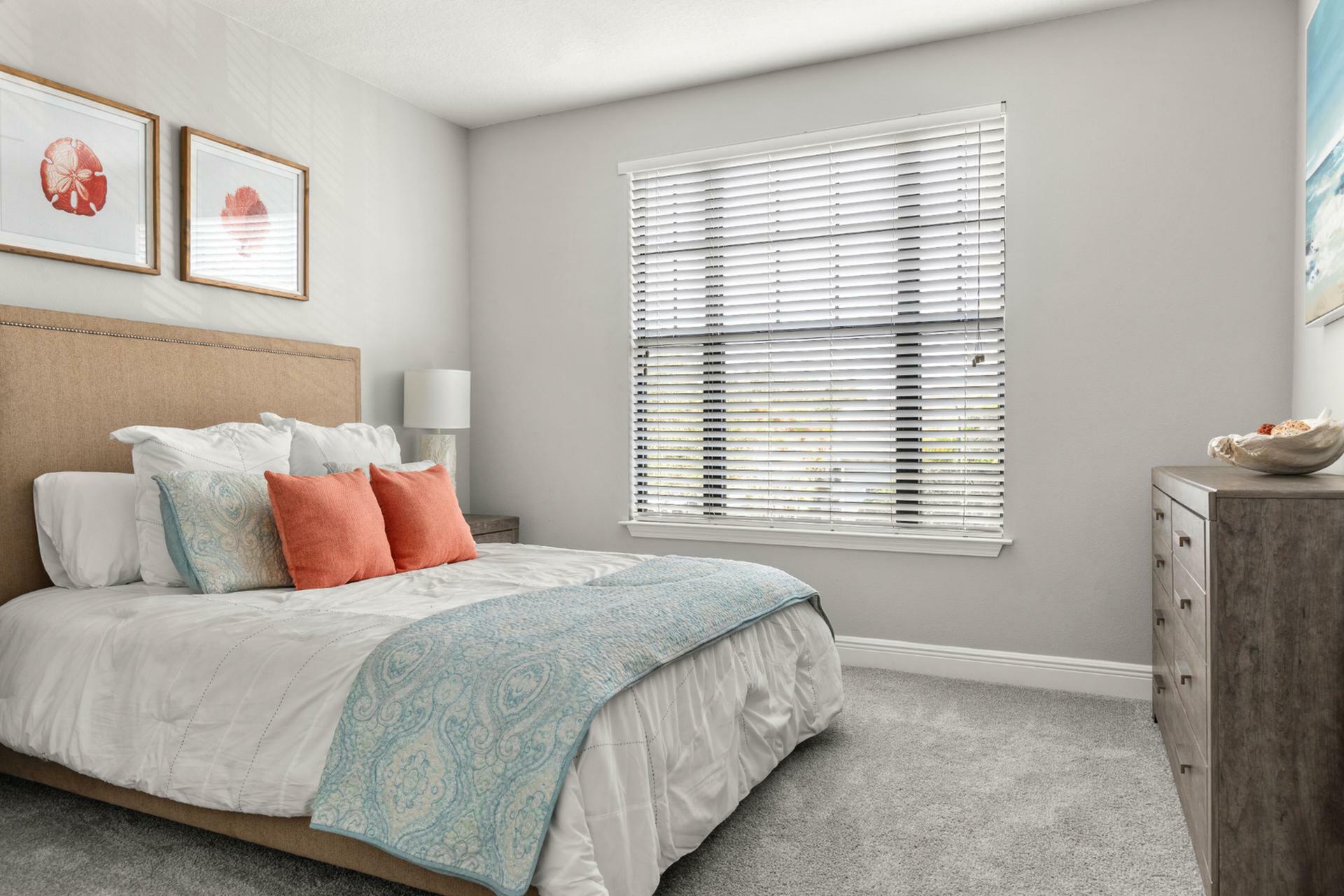 Bright and inviting bedroom with a stylish bed, plush pillows, and soft natural light filtering through window blinds, creating a cozy and welcoming atmosphere.