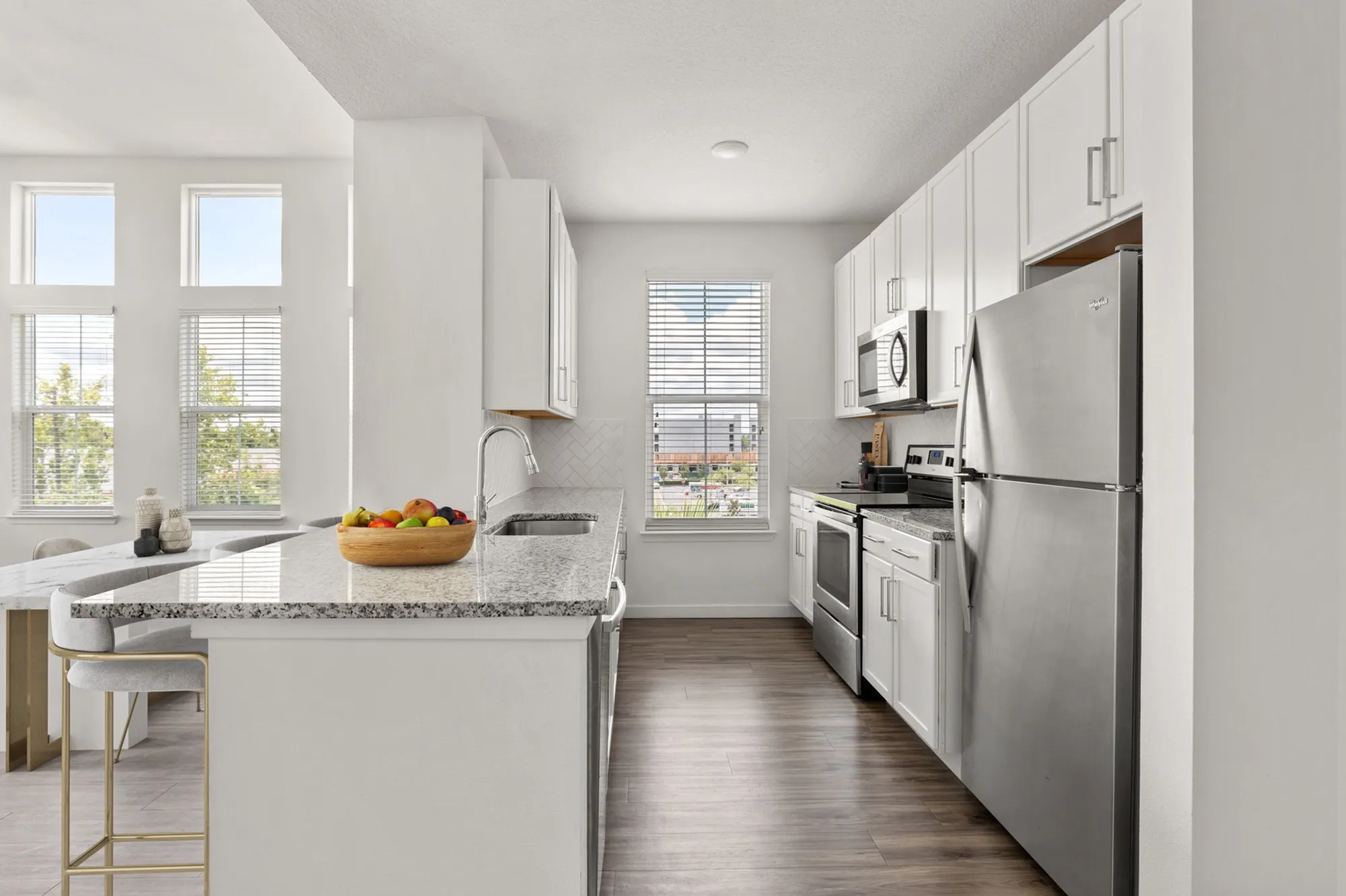 Furnished kitchen with large counter, sink, white cabinets, and stainless steel appliances