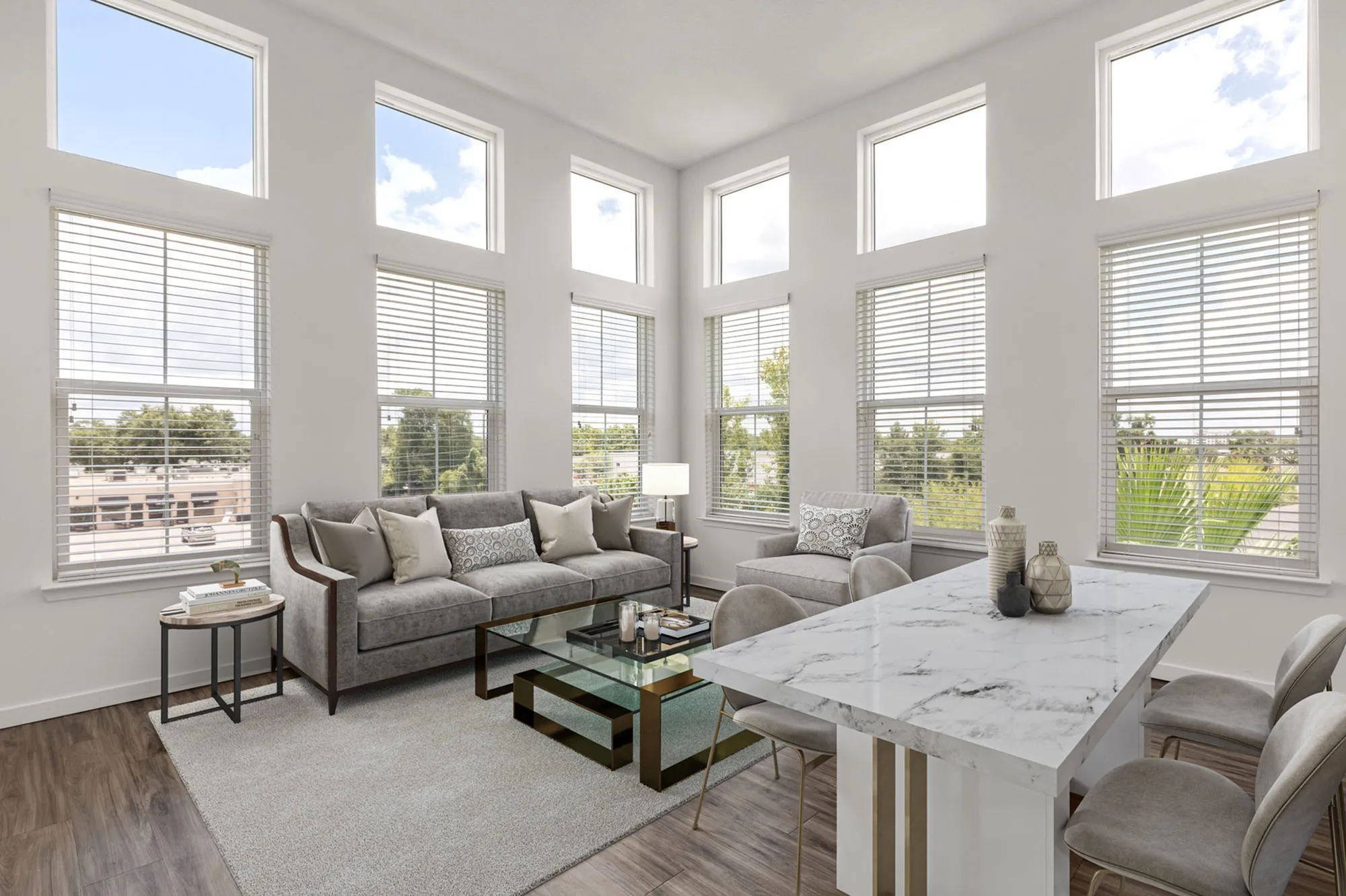 Furnished living area with six windows, grey couches, and a view of a dining table.