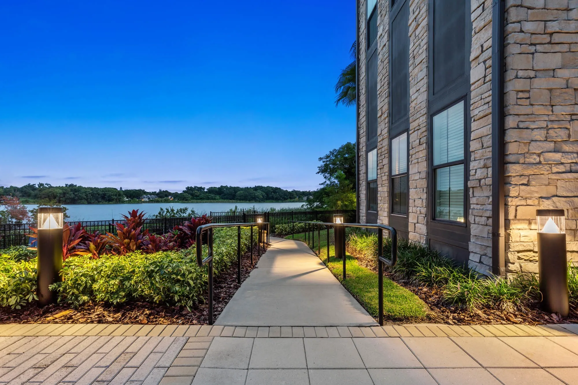 Paved lit walkway outside of apartment at night with shrubbery and railing