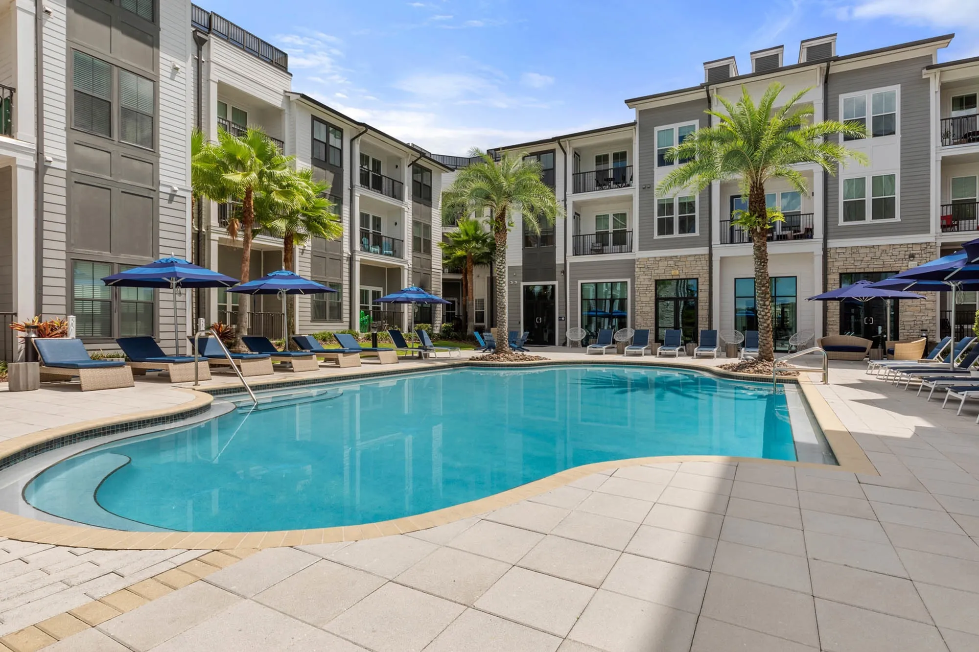 Outdoor pool in the daytime surrounded by poolside chairs, large umbrellas and palm trees