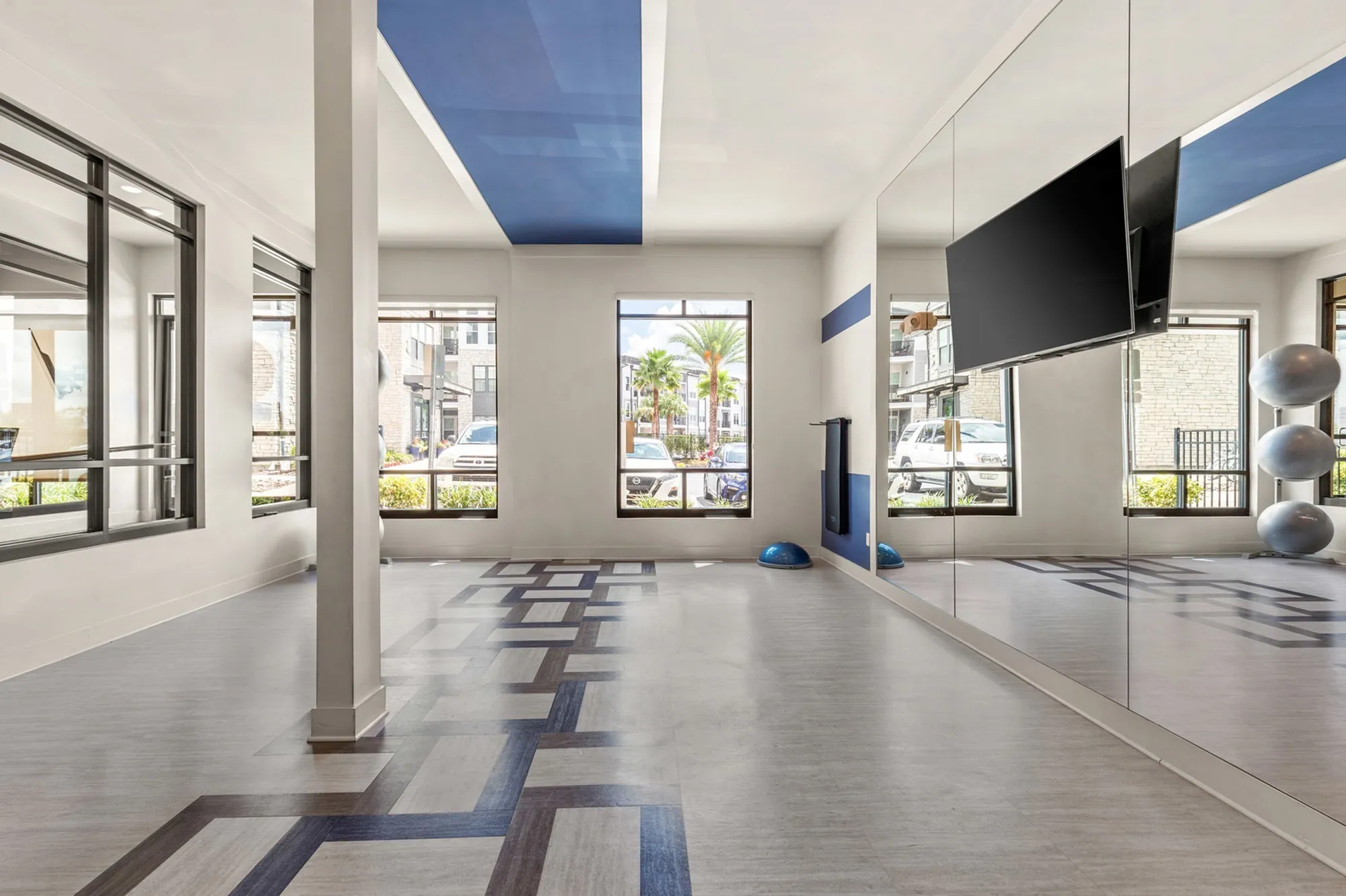 Open floor indoor fitness area with mirrors on one wall and windows
