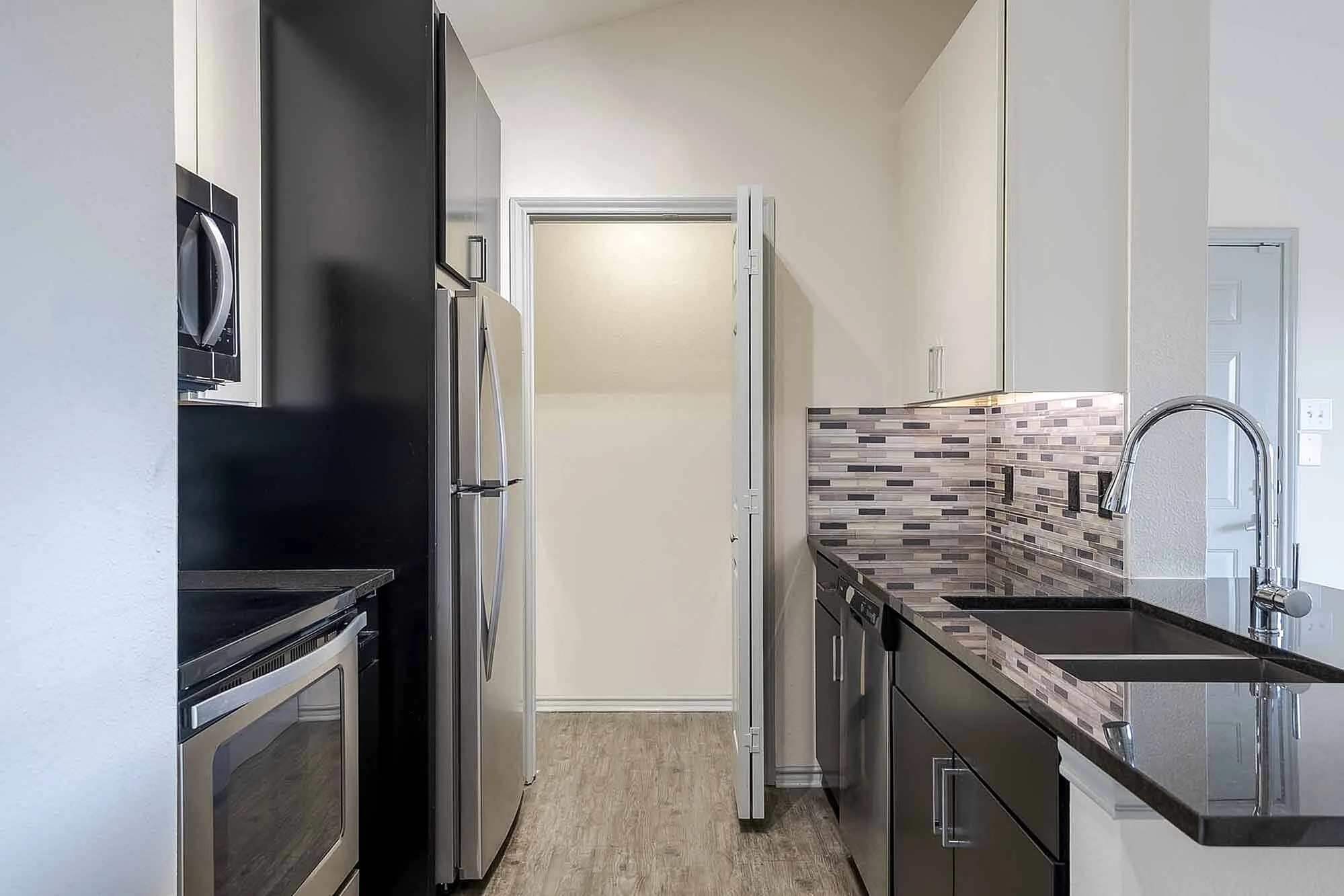 Modern kitchen with sleek stainless steel appliances, mosaic tile backsplash, and elegant black countertops.