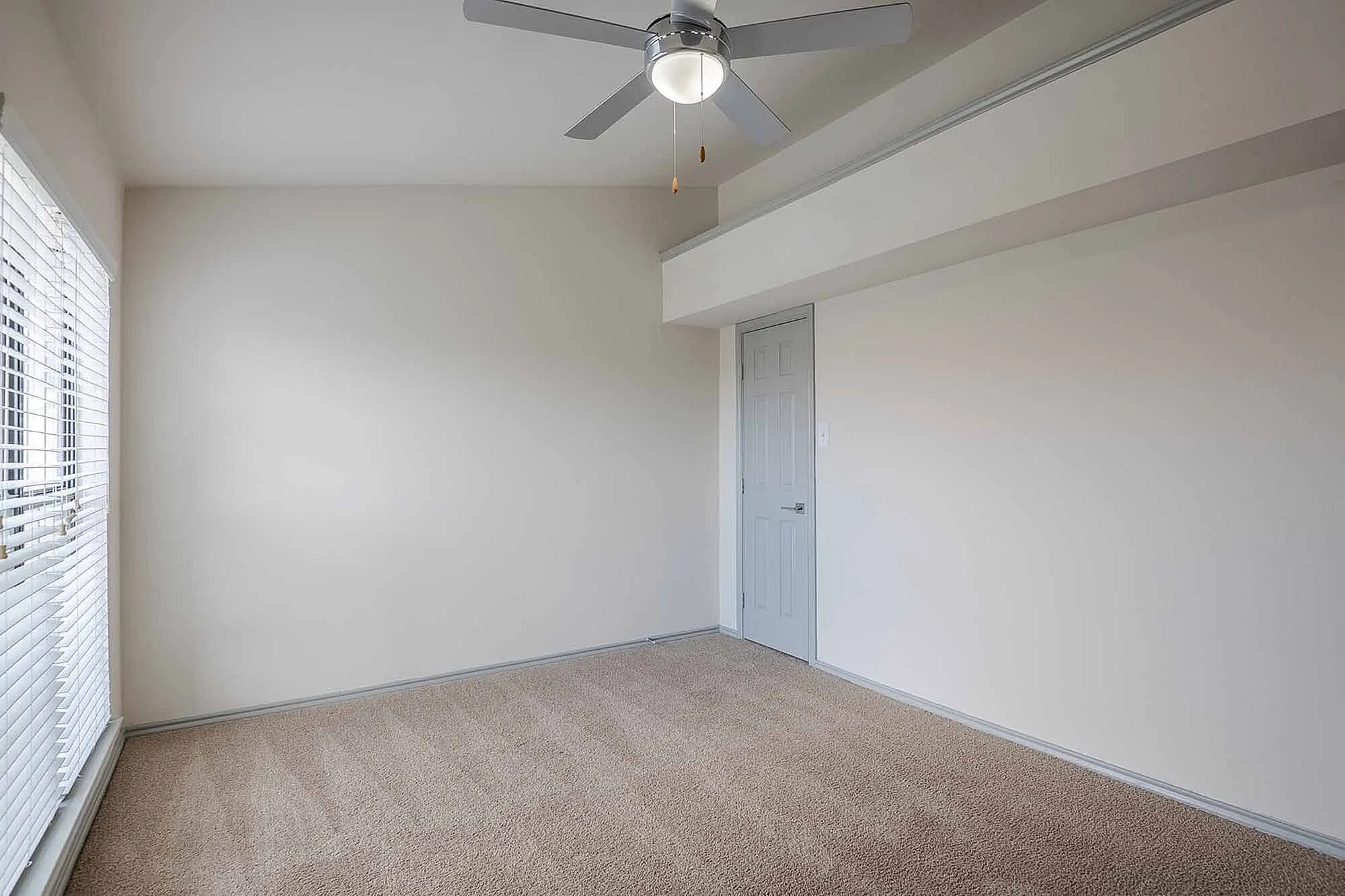 Bright and airy room with plush carpeting and elegant ceiling fan, perfect for comfort and relaxation.