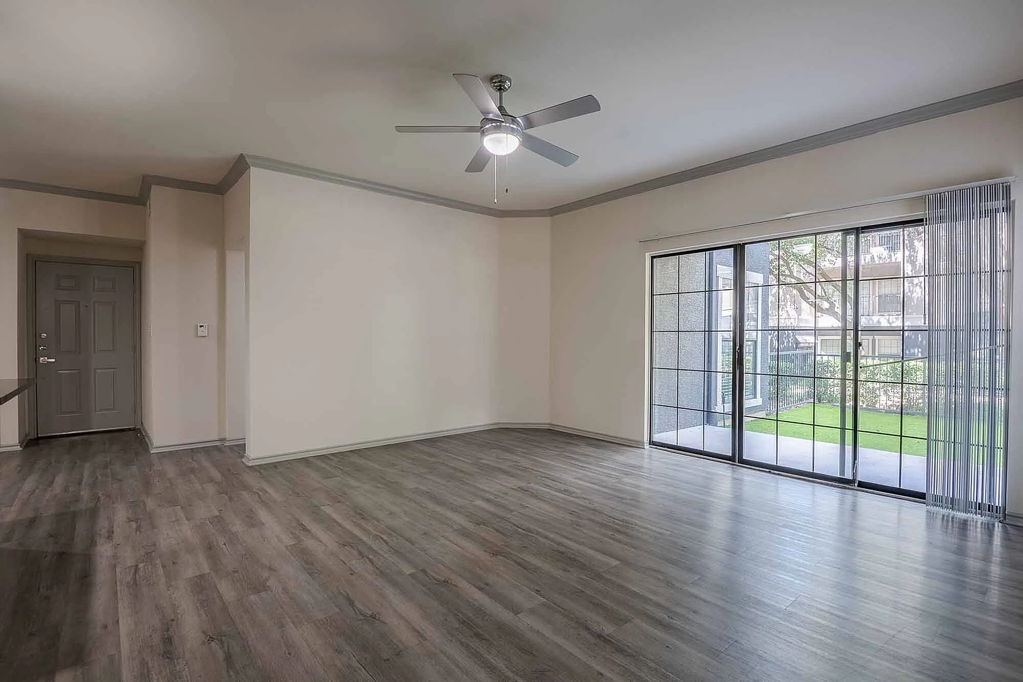 Inviting living room with elegant laminate flooring, modern ceiling fan, and large glass doors leading to a lush green patio.