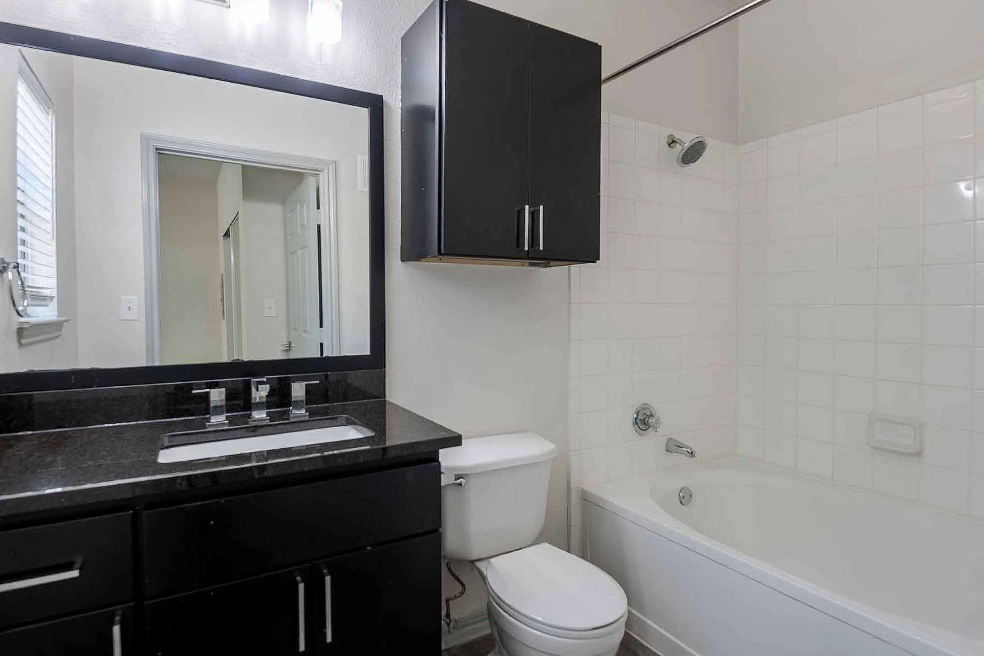 Modern bathroom with sleek black cabinetry, elegant granite countertop, and a pristine white bathtub for a luxurious feel.