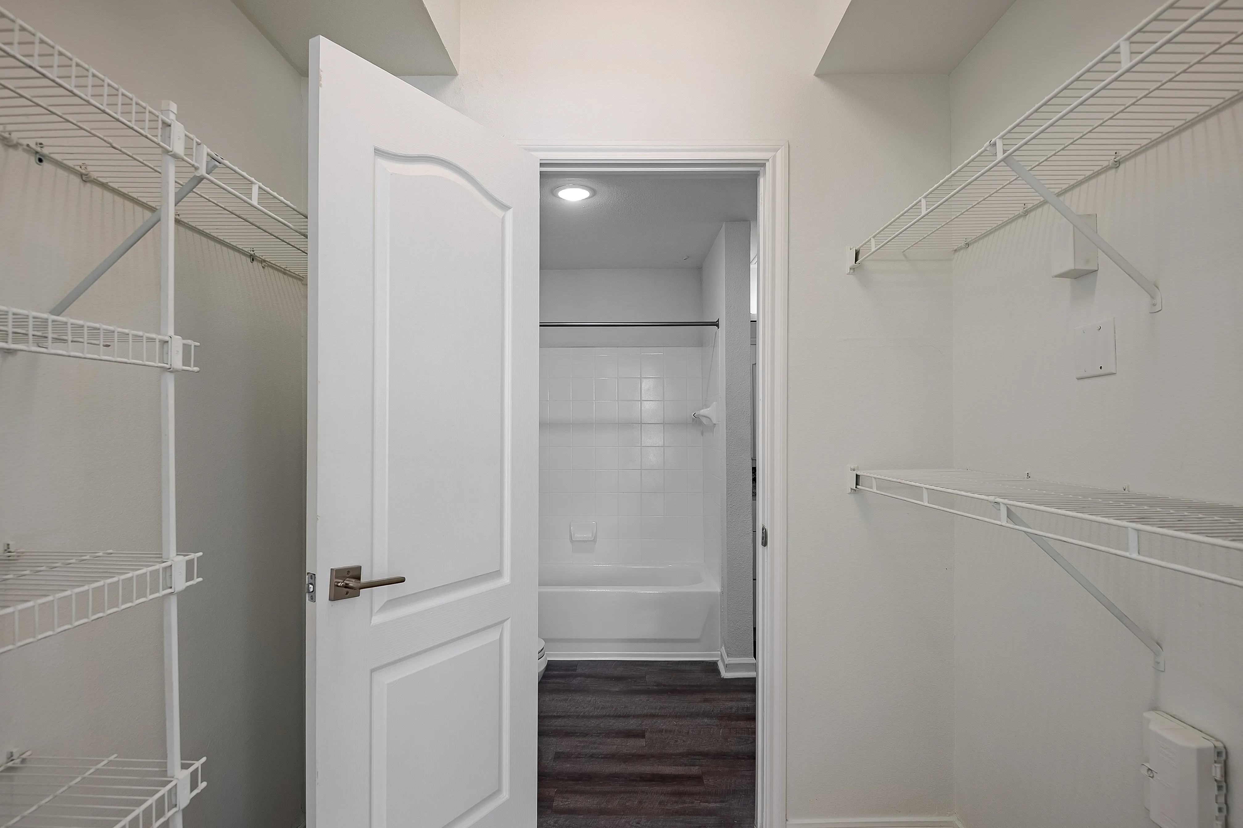 Inviting apartment interior showcasing a spacious closet with modern wire shelving adjacent to a pristine white tiled bathroom.