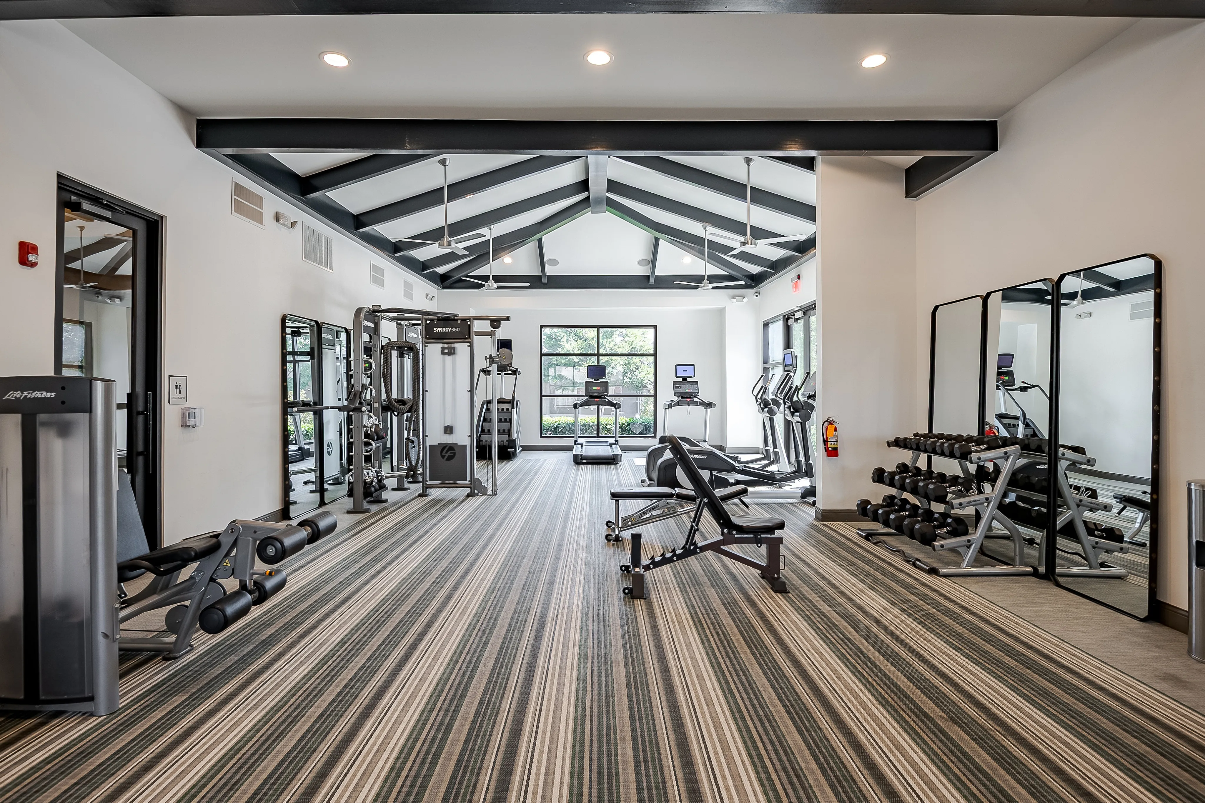 Modern fitness center with state-of-the-art equipment, mirrored walls, and sleek striped flooring, ideal for a comprehensive workout.