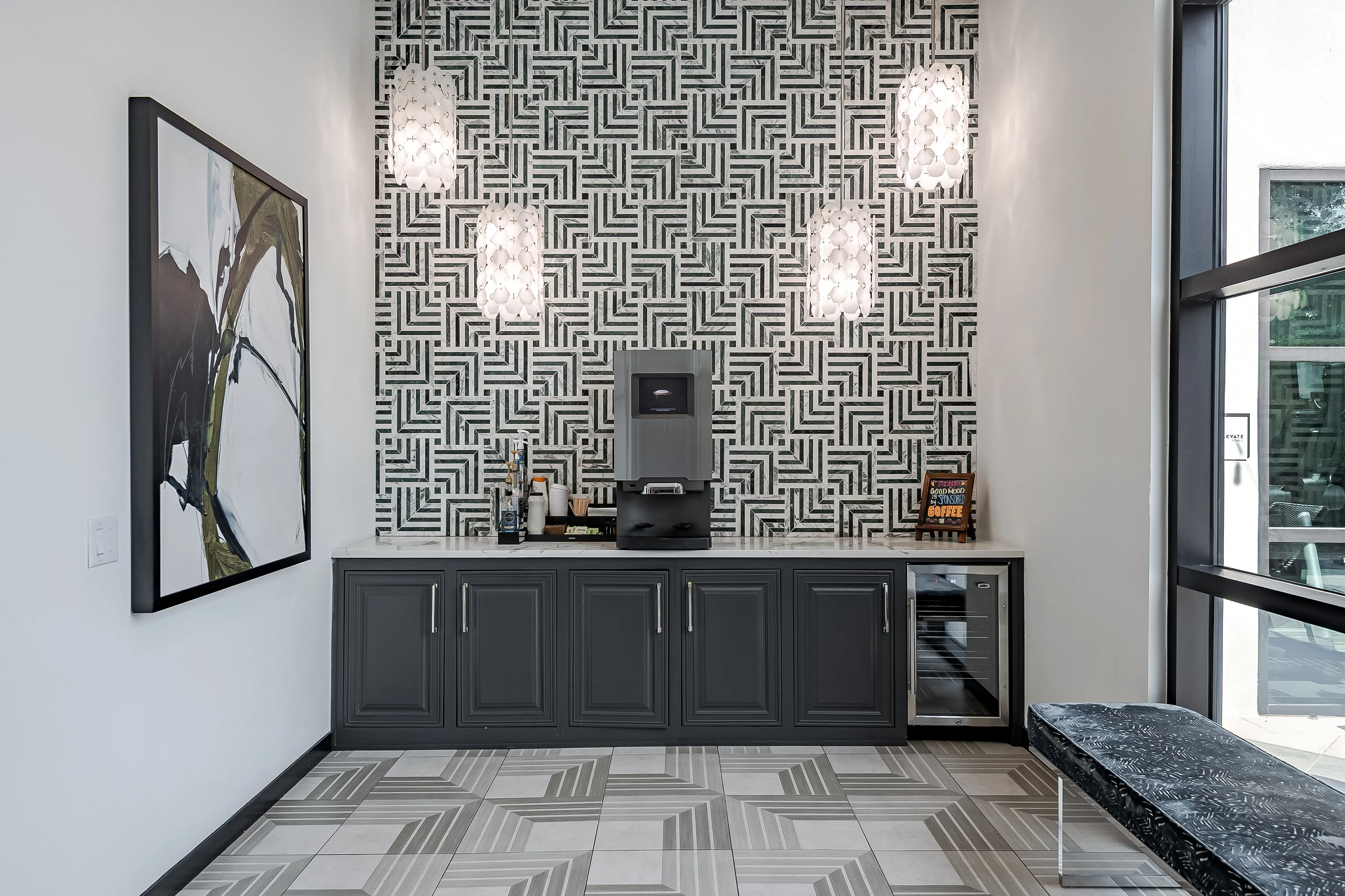 Chic coffee station with patterned backsplash, elegant lighting, and modern cabinetry in a stylish apartment.