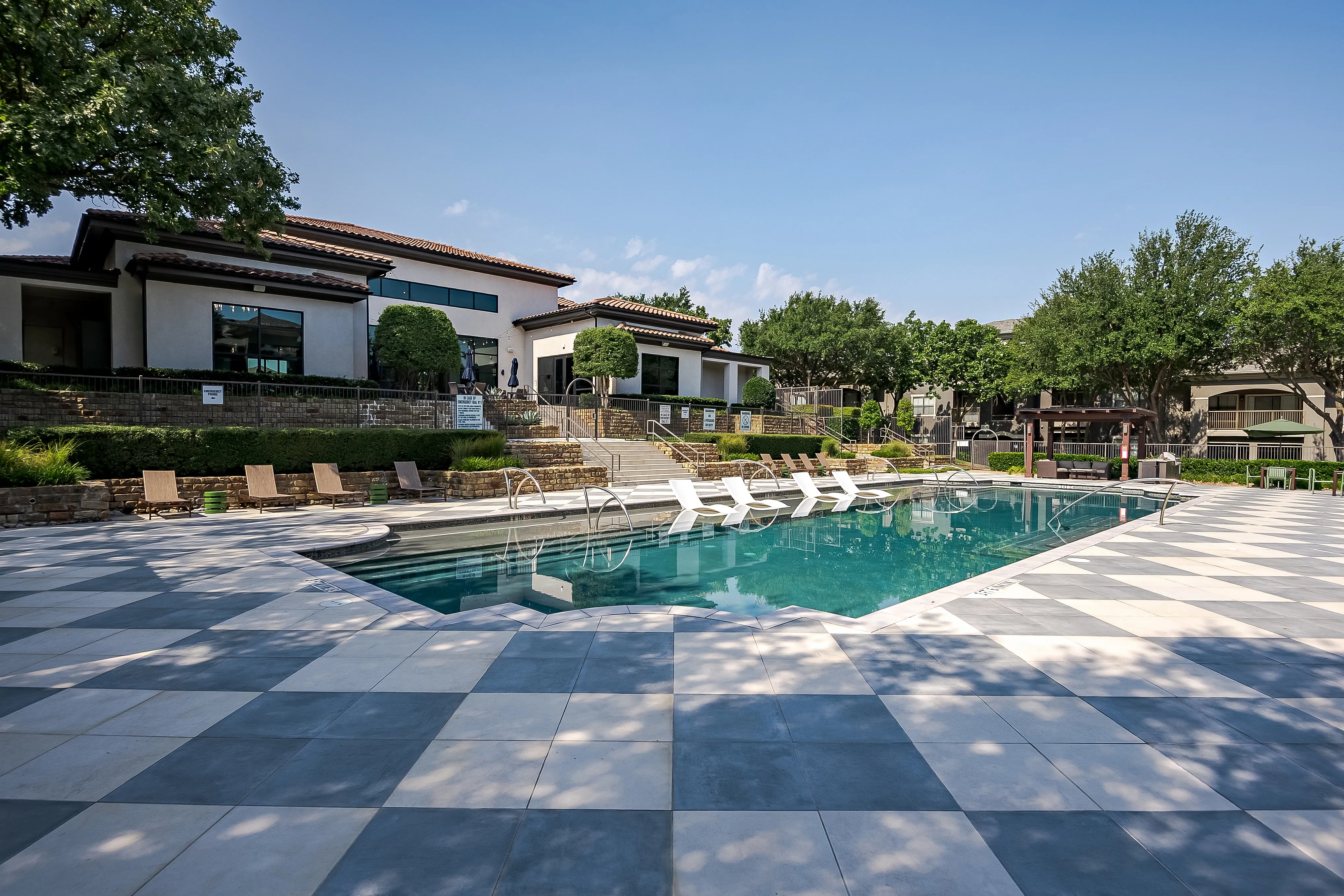 Luxurious outdoor swimming pool with stylish lounge chairs, surrounded by lush greenery and modern buildings, perfect for relaxation and leisure.