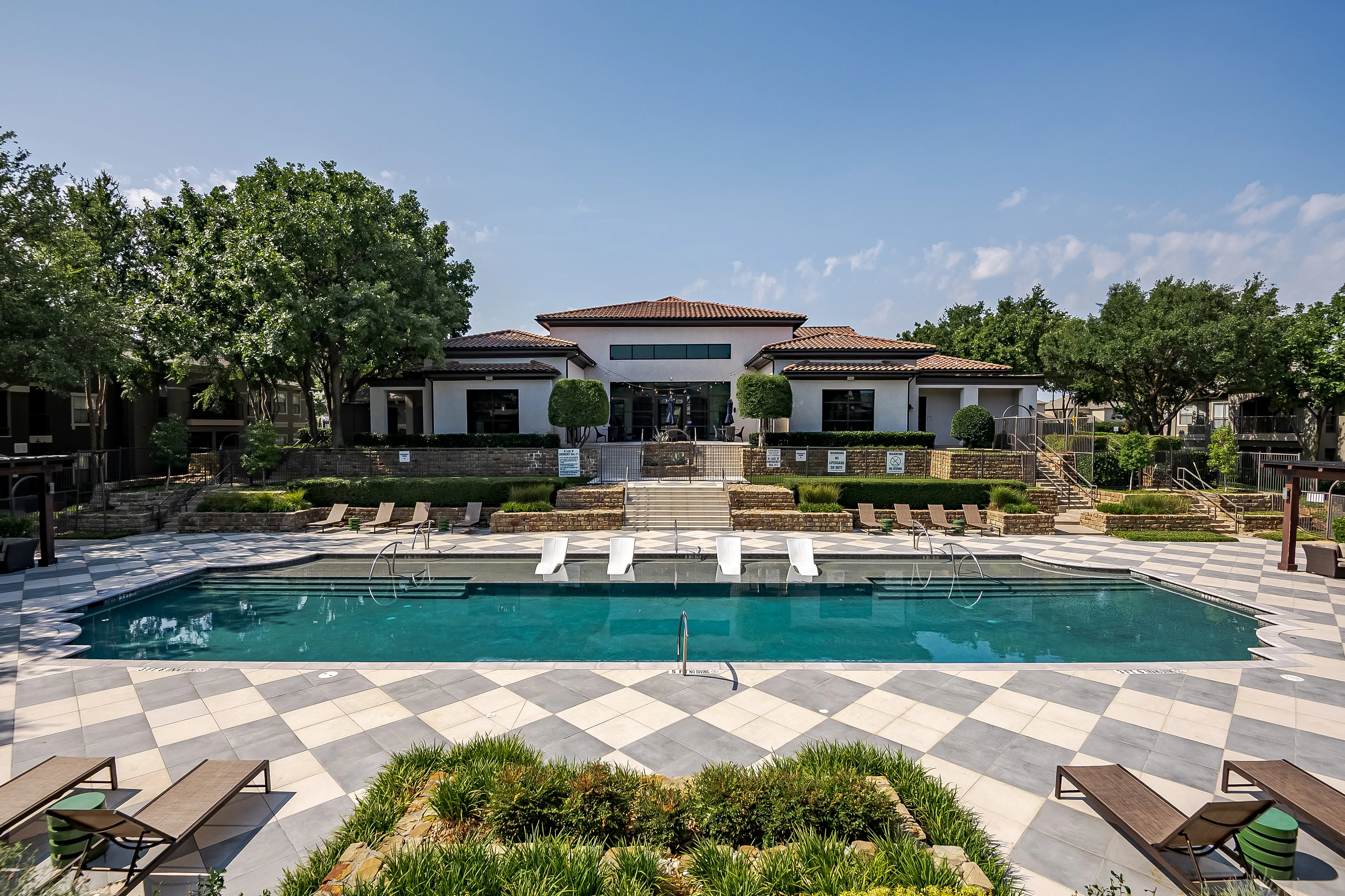 Luxury apartment complex with a stunning outdoor pool, surrounded by lush landscaping and elegant modern architecture.