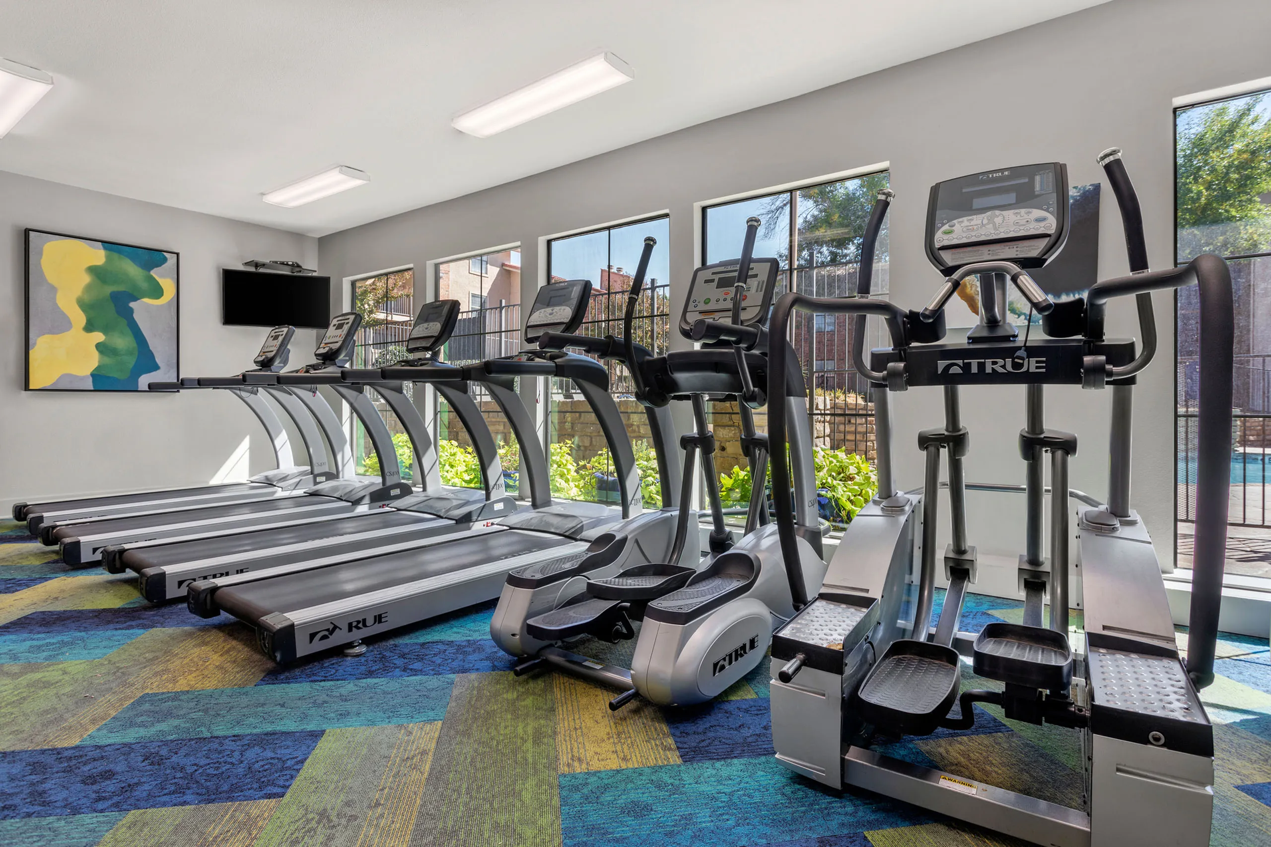 Modern fitness center with sleek treadmills and elliptical machines facing large windows with a refreshing pool view.