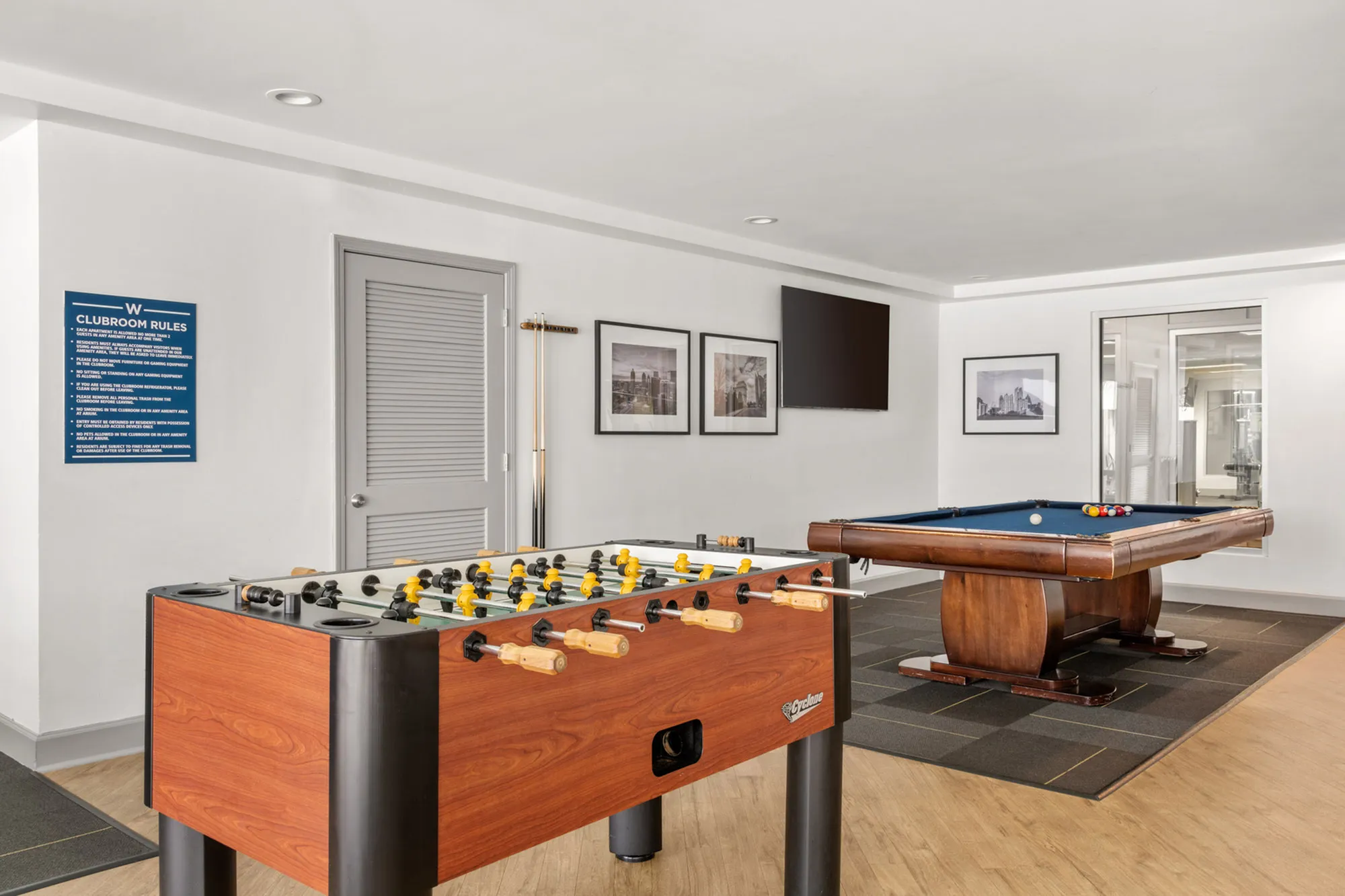 Modern recreational room with a chic foosball table and elegant billiards table, complemented by stylish decor and wood flooring.