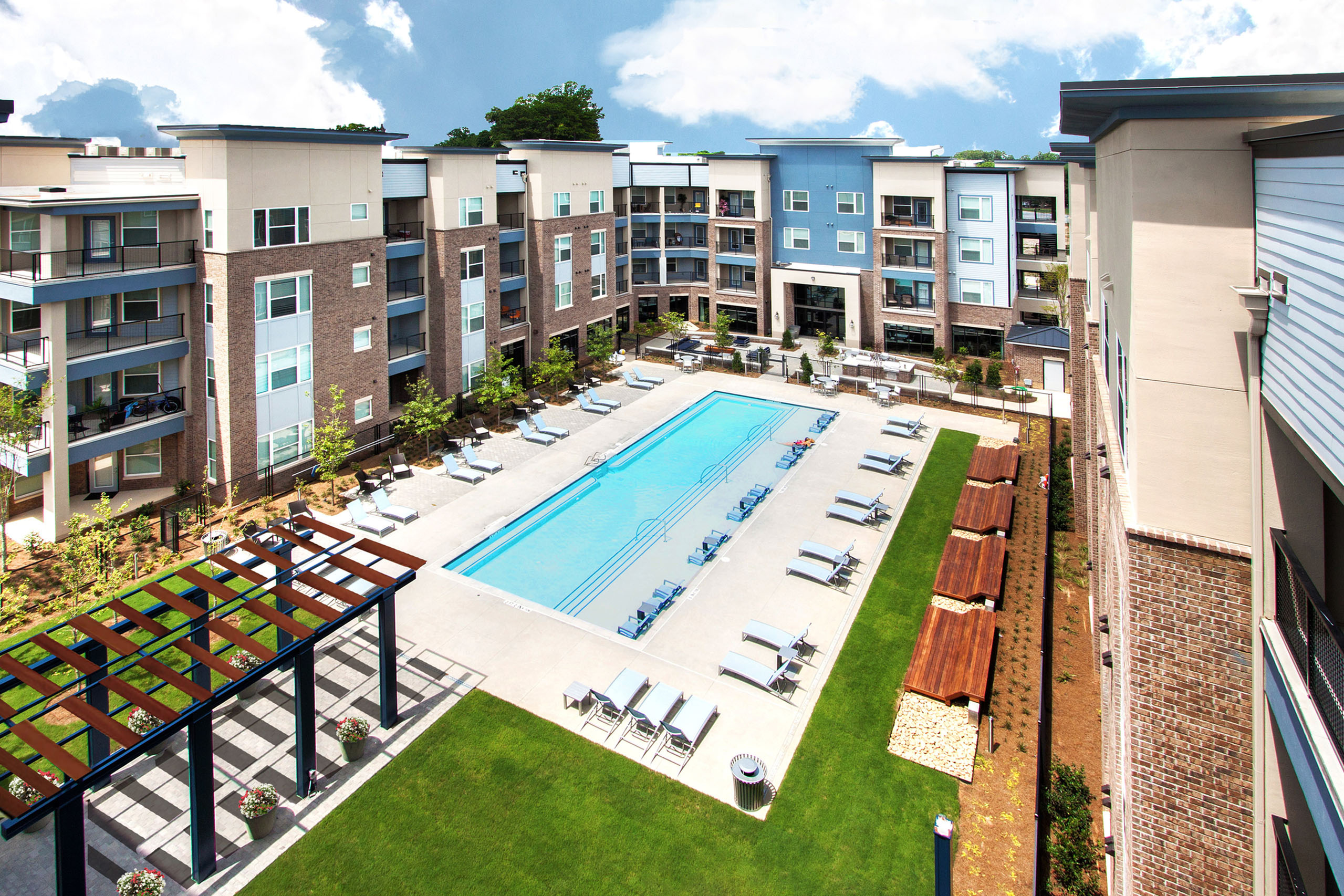 Modern apartment complex with a vibrant courtyard featuring a large swimming pool, lush green lawns, and cozy seating areas.