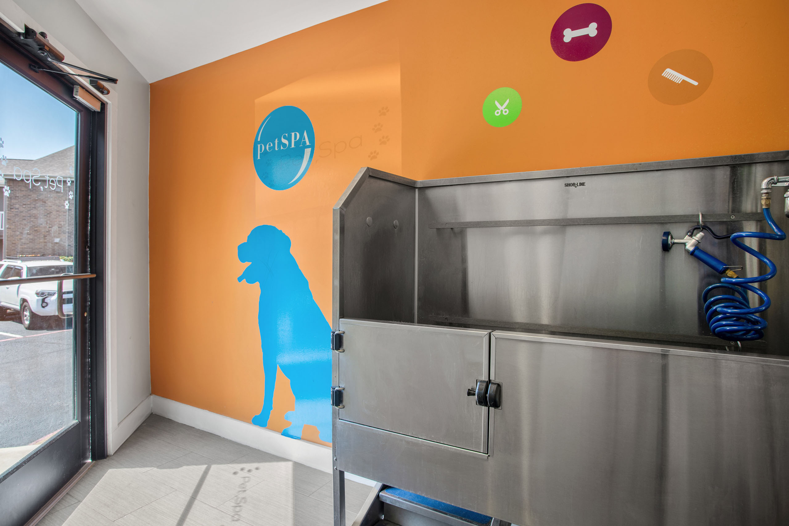 Bright pet spa with cheery orange walls, featuring modern grooming equipment and playful dog silhouette decor.