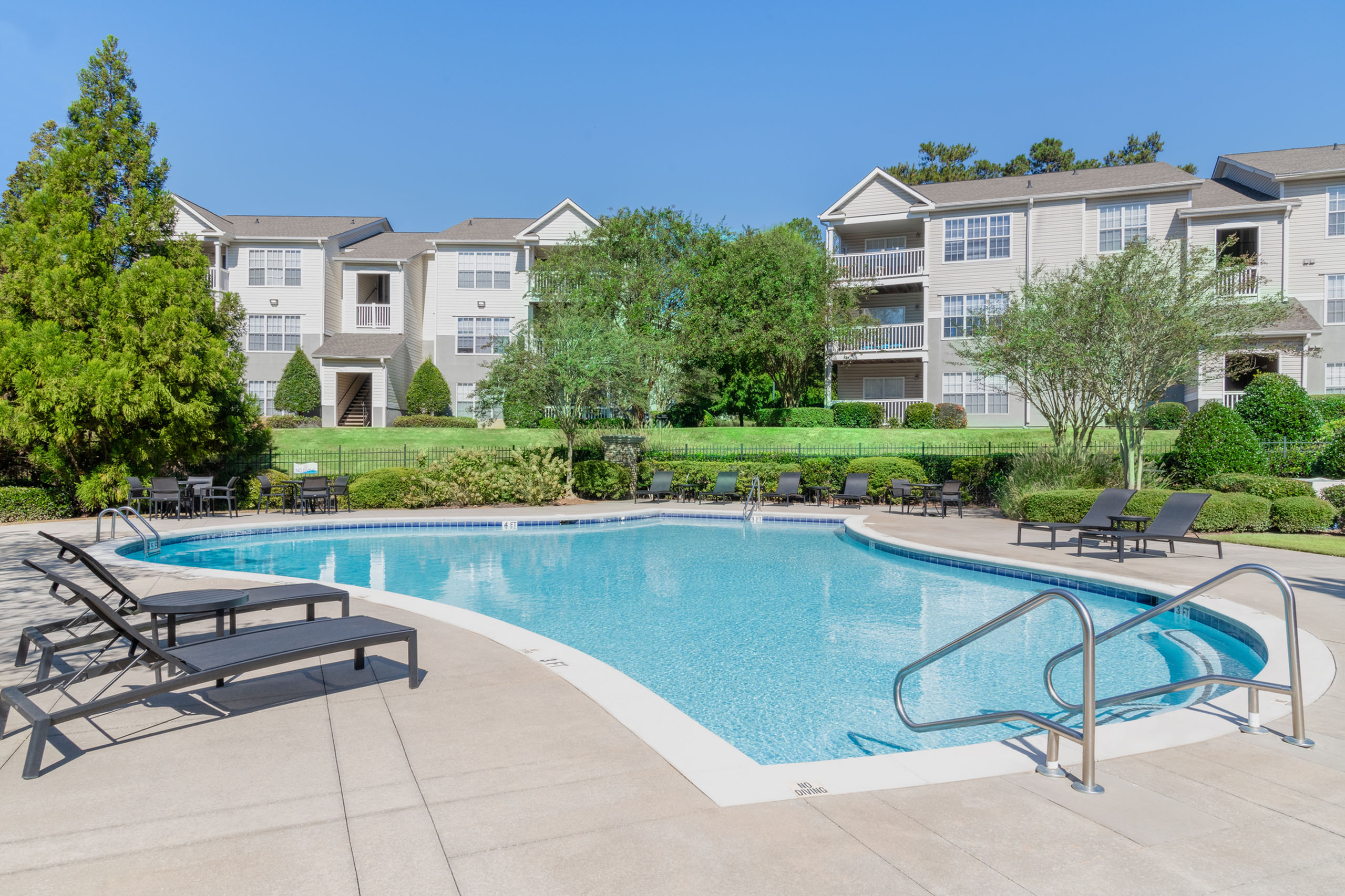 Inviting apartment complex with a sparkling pool and lush greenery, offering a serene retreat for residents.