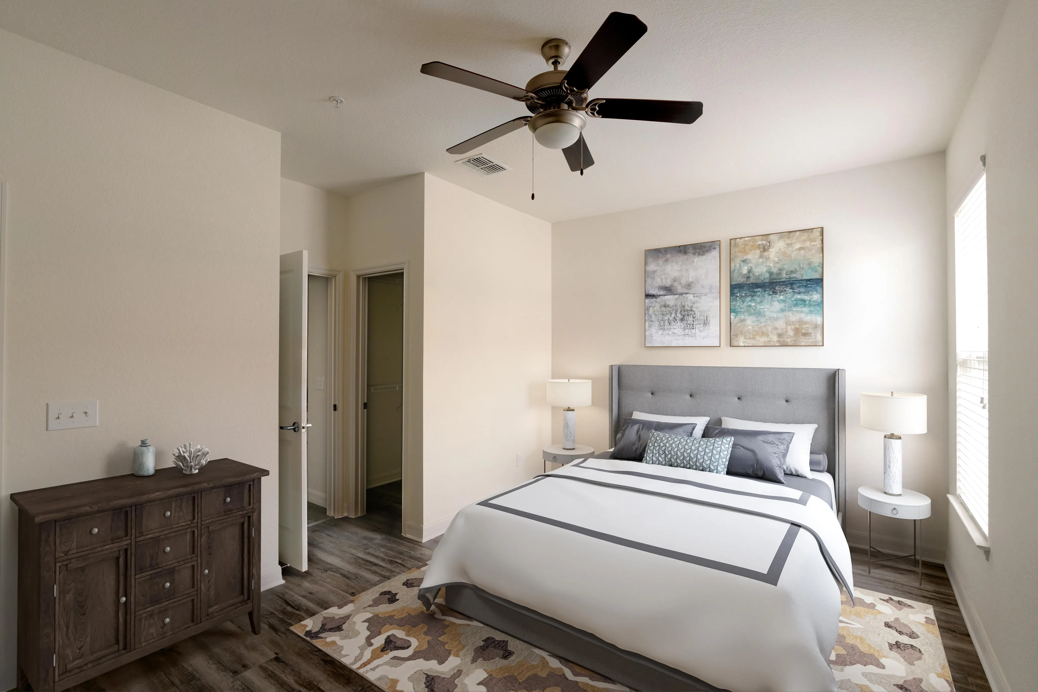 Elegant bedroom with a plush gray upholstered bed, modern wooden dresser, and stylish ceiling fan, offering a serene and inviting atmosphere.