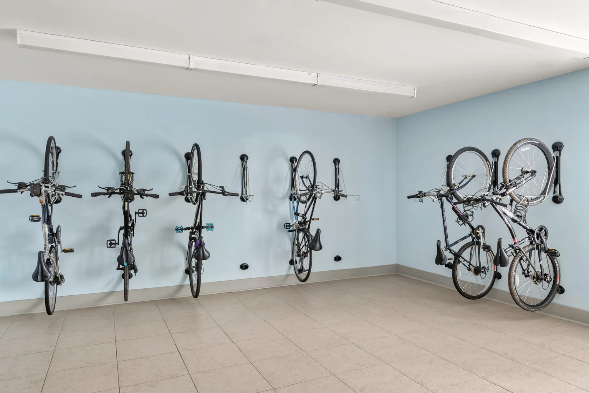 Modern bike storage area with wall-mounted racks and neatly organized bicycles on a tiled floor.