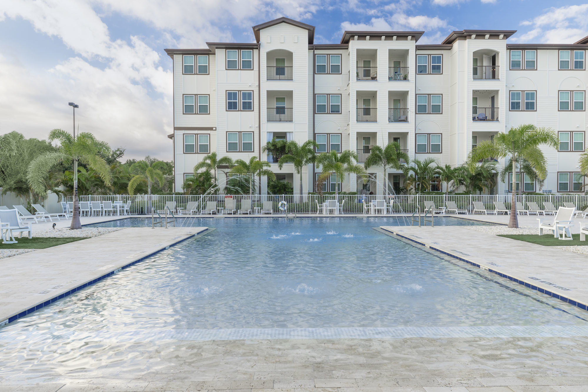 Luxury apartment complex with a sparkling pool, surrounded by palm trees and modern balconies, offering a resort-style living experience.