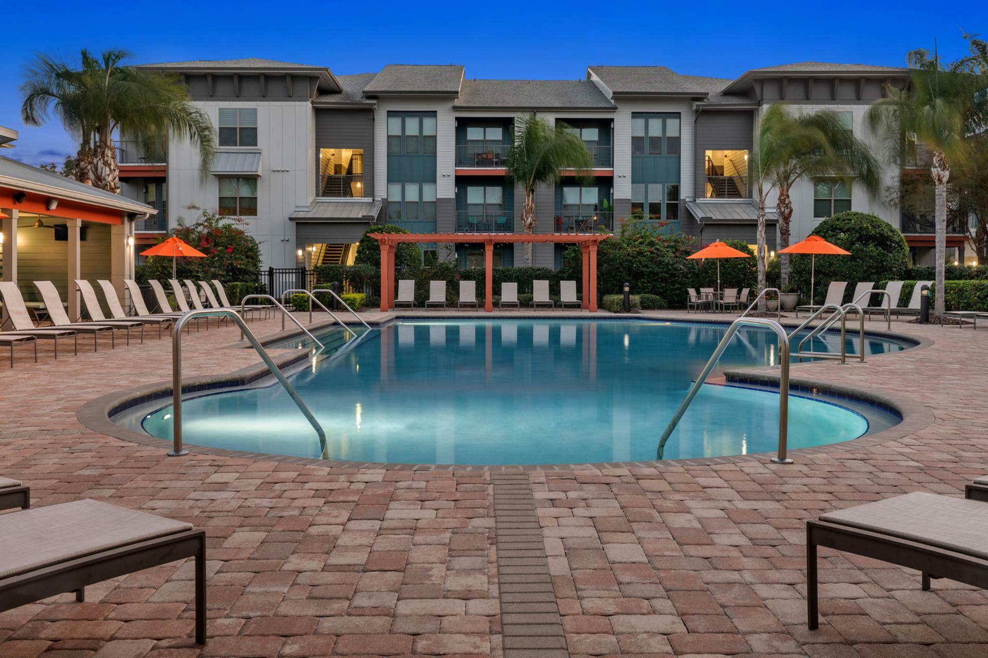 Elegant apartment complex featuring a pristine pool with stylish lounge chairs and vibrant landscaping, perfect for relaxation and leisure.