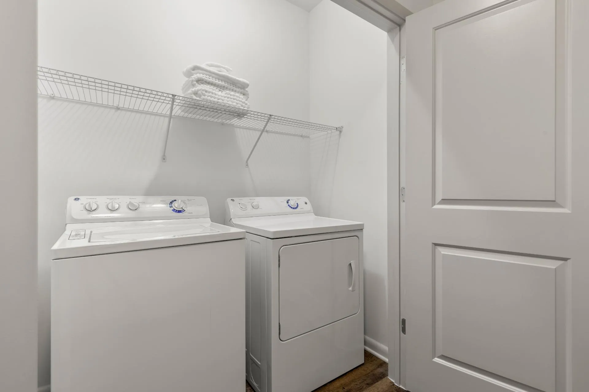 Modern laundry room with efficient washer and dryer, featuring sleek white design and cozy shelving.
