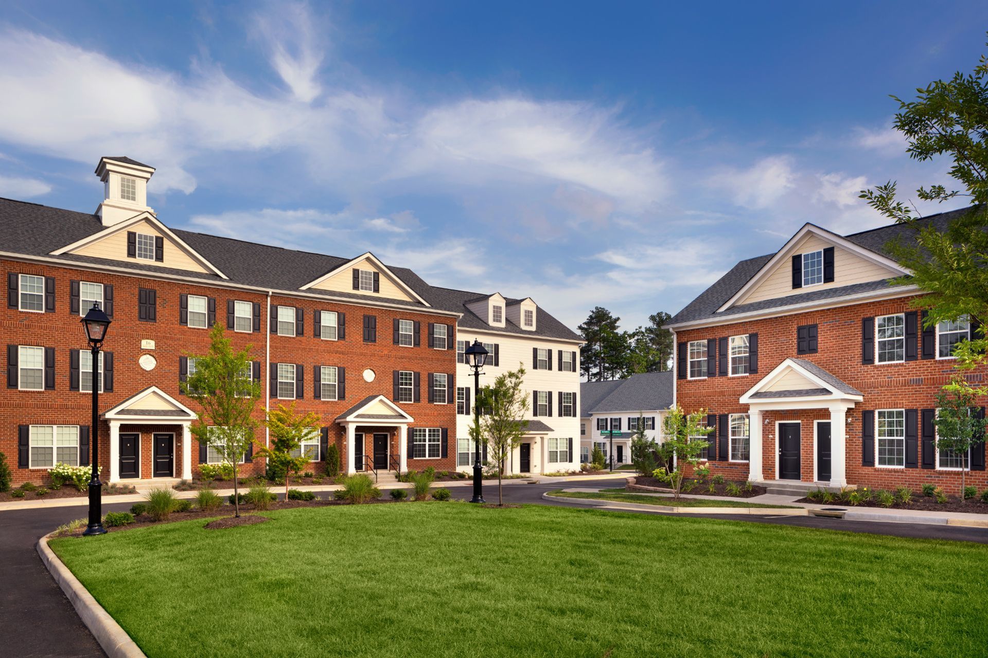 Charming colonial-style apartment complex with brick facades, lush green lawn, and picturesque surroundings.